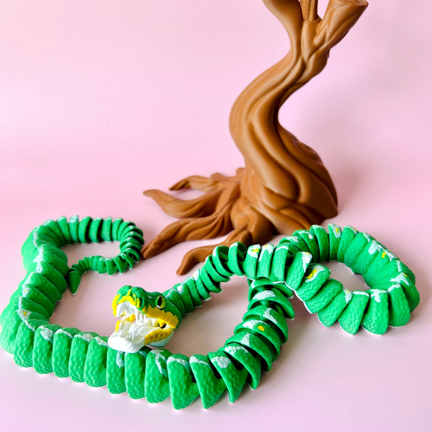 A green serpent with a white and yellow face coils around a brown, twisted tree against a pink background.