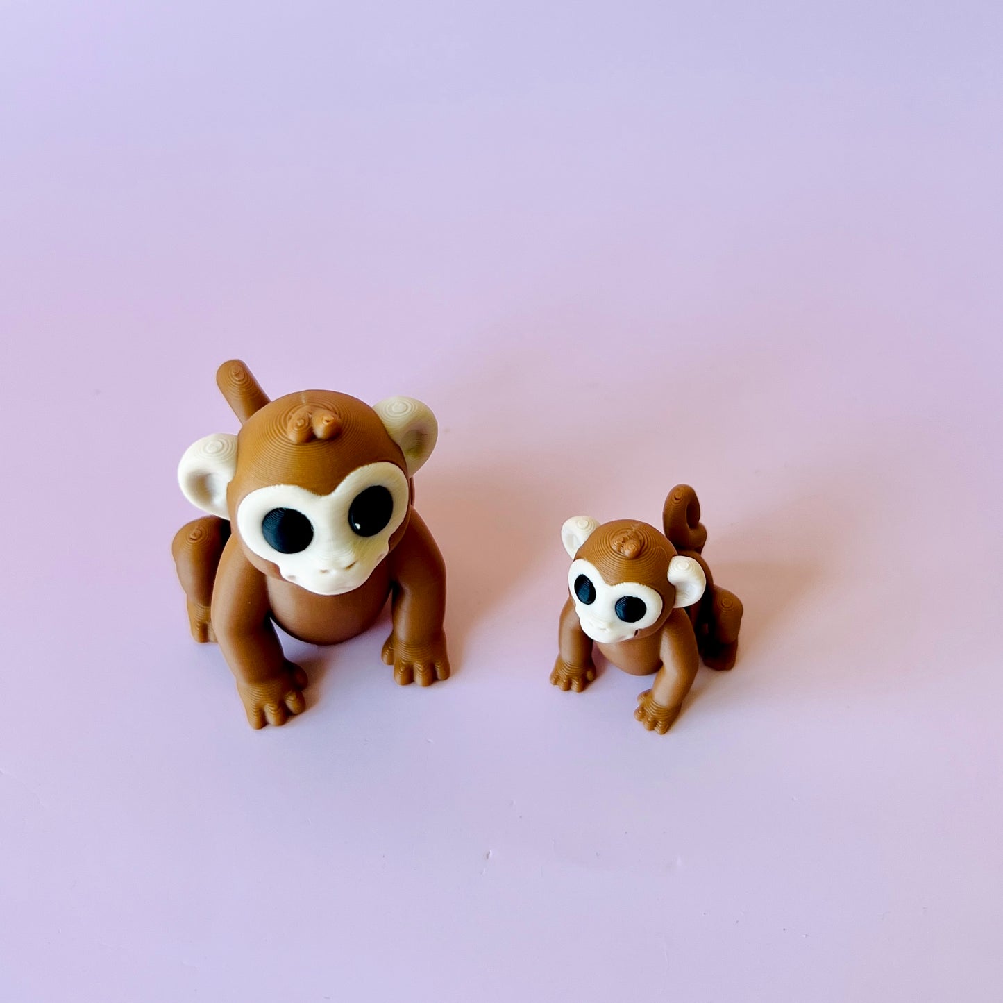 Two cute, brown monkey figures with large eyes, one smaller than the other, set against a soft pink background.