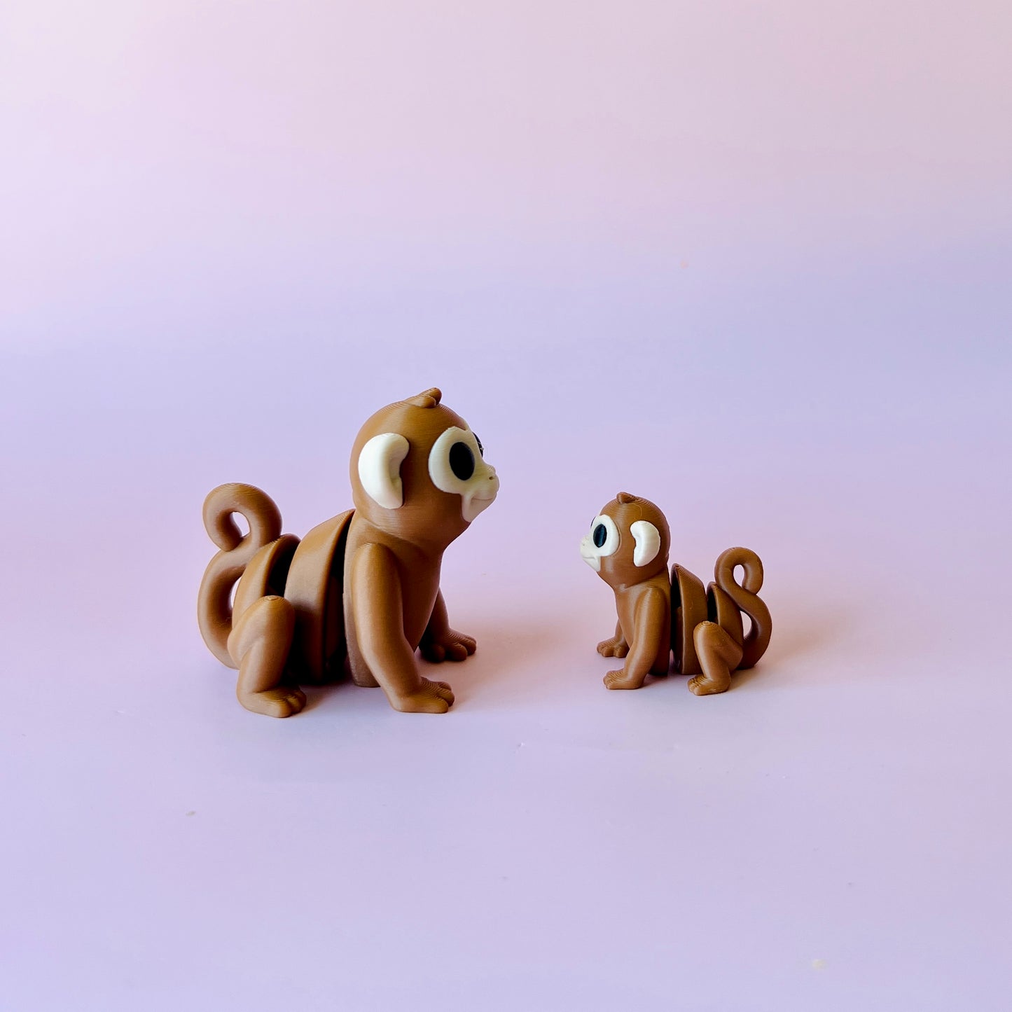 Two cartoon-like monkeys, one larger and one smaller, sit on a soft pink background, gazing at each other.