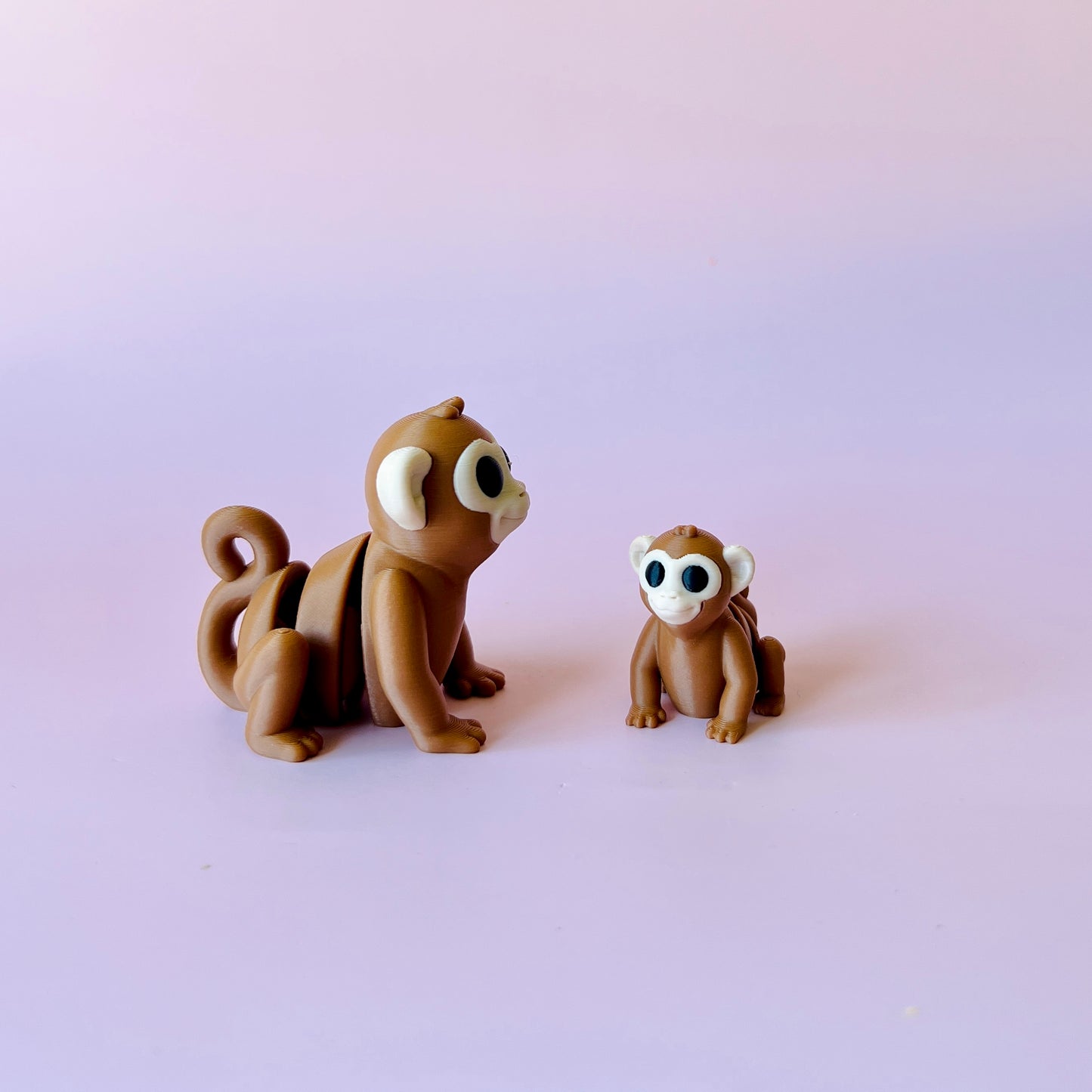 Two whimsical brown monkeys with large eyes sit against a soft pastel background, showcasing playful expressions.
