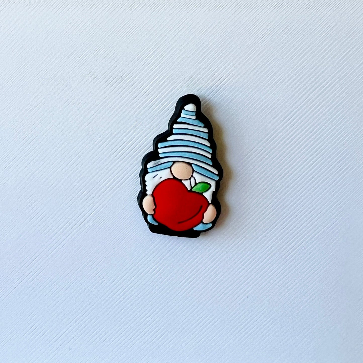 A whimsical character with a blue striped hat holds a bright red apple against a textured white background.