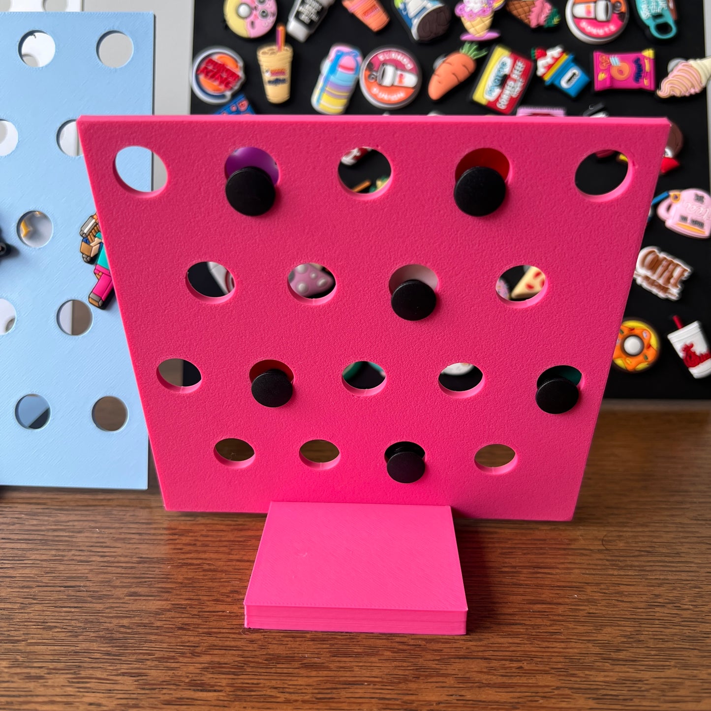Vibrant pink display stand with holes for showcasing charms, featuring a sleek base and a backdrop of colorful charm designs.