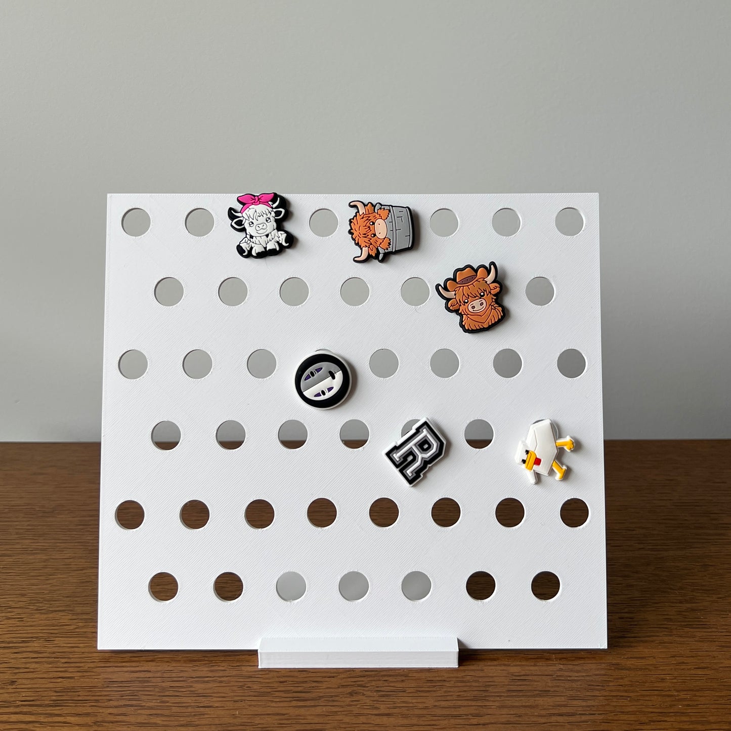 Display stand showcasing colorful shoe charms on a white perforated base, perfect for organizing and highlighting collections