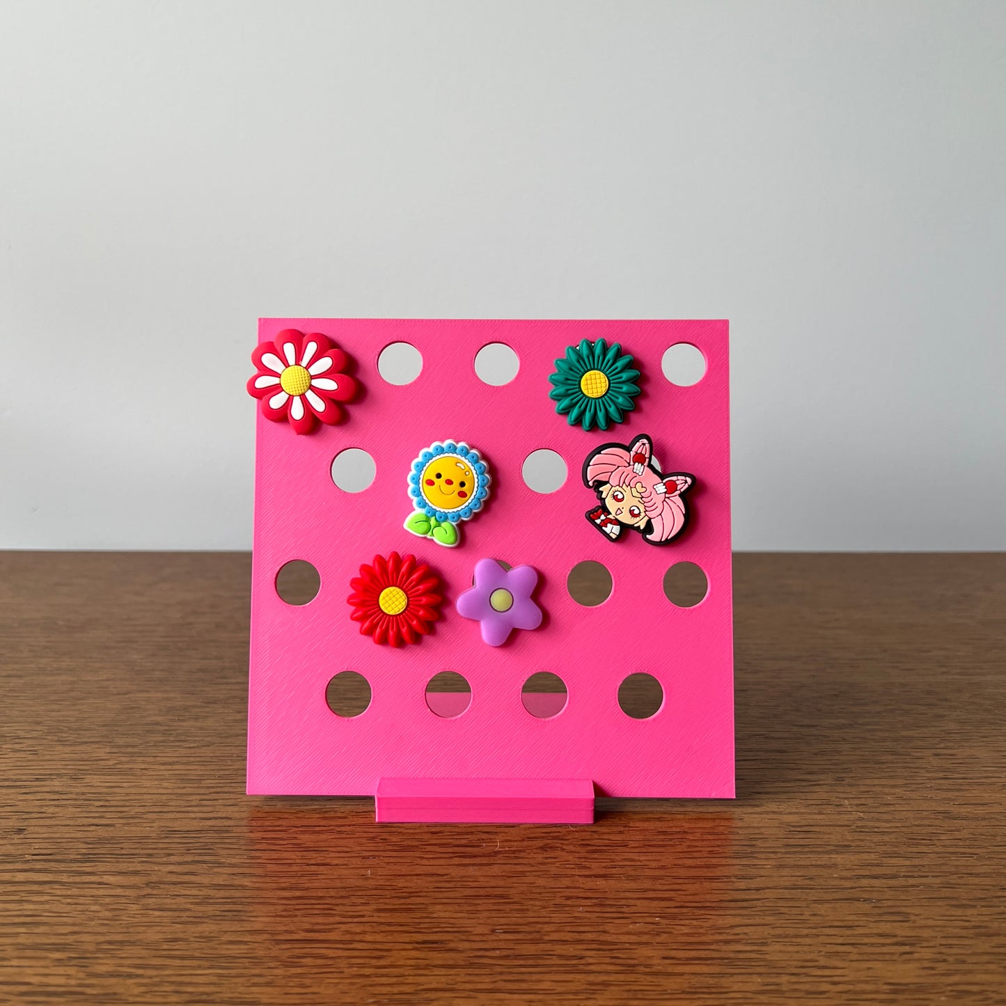Vibrant pink display stand showcasing colorful charms with floral designs and a playful character, ideal for charm enthusiast