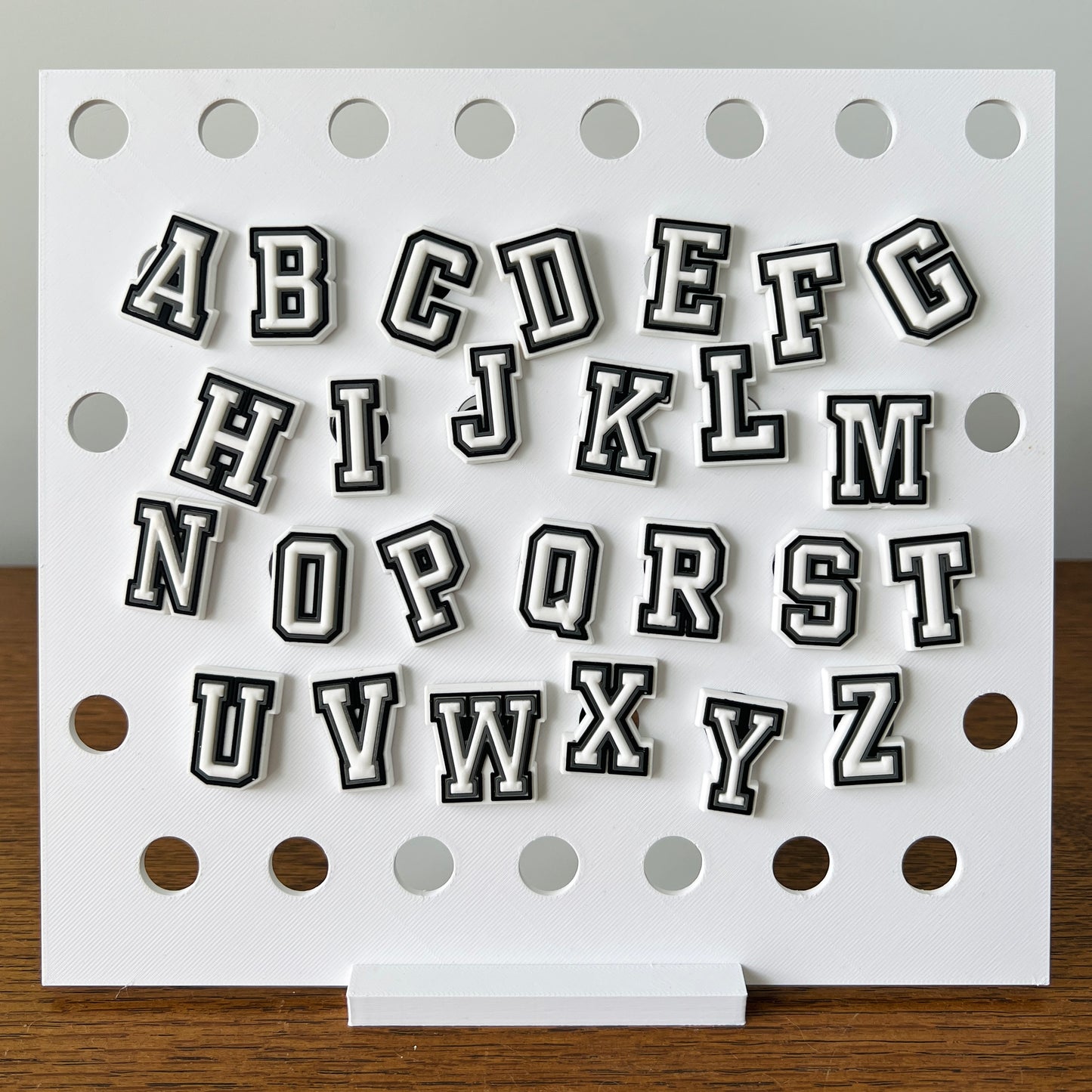 Black and white alphabet shoe charms displayed on a white board, showcasing letters A to Z in a playful, bold style.