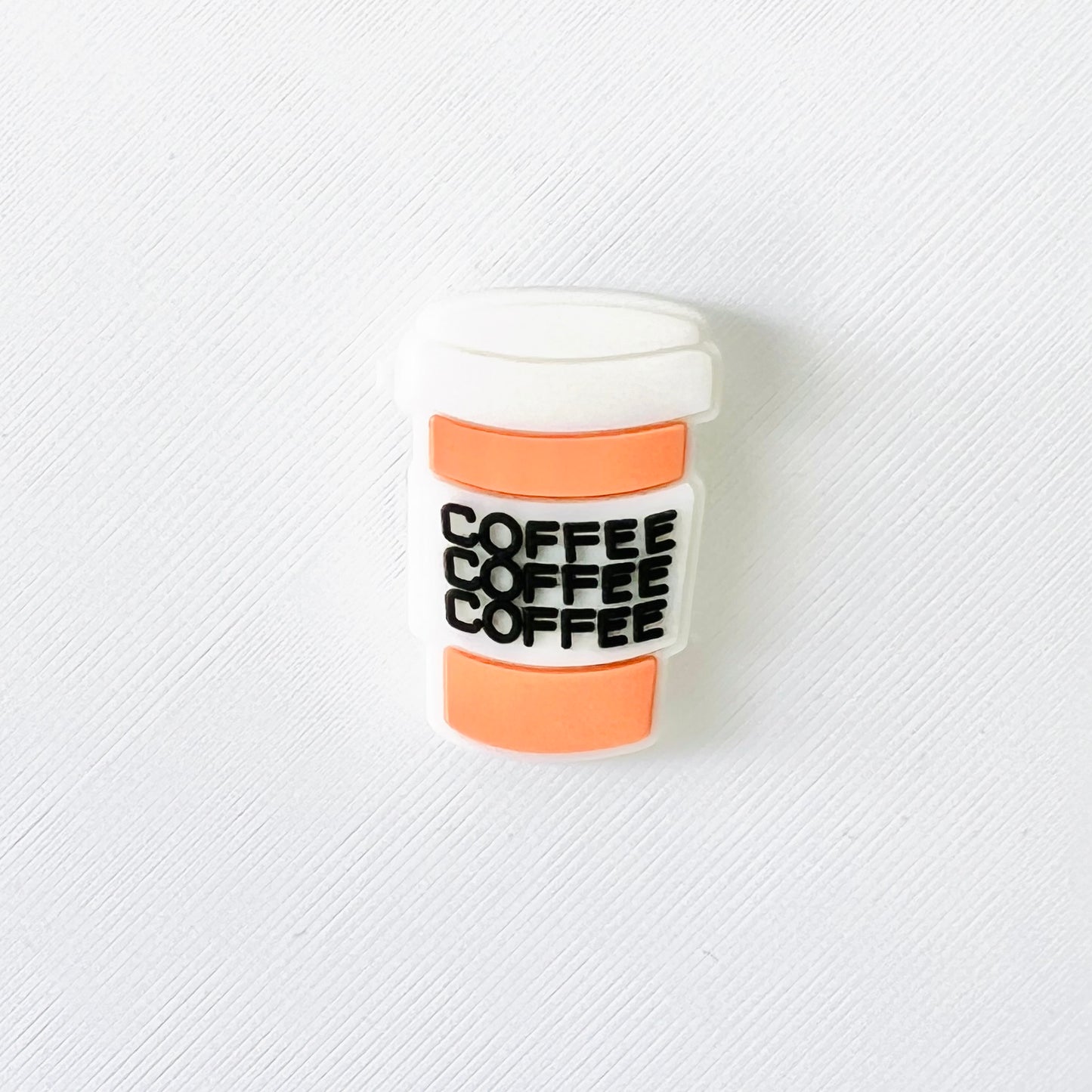 A two-tone shoe charm shaped like a coffee cup with "coffee" printed three times in bold black letters.