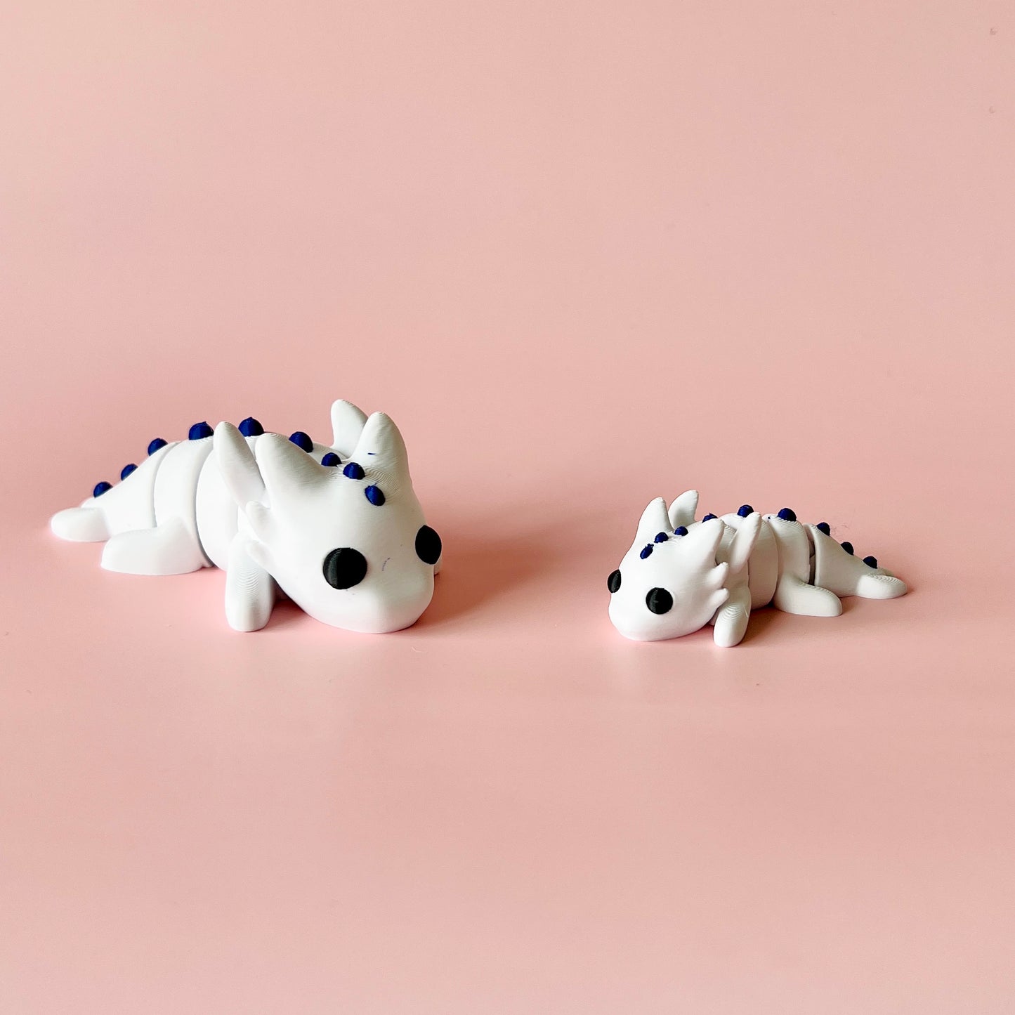 Two small white creatures with black eyes and blue spikes, resting on a soft pink background.
