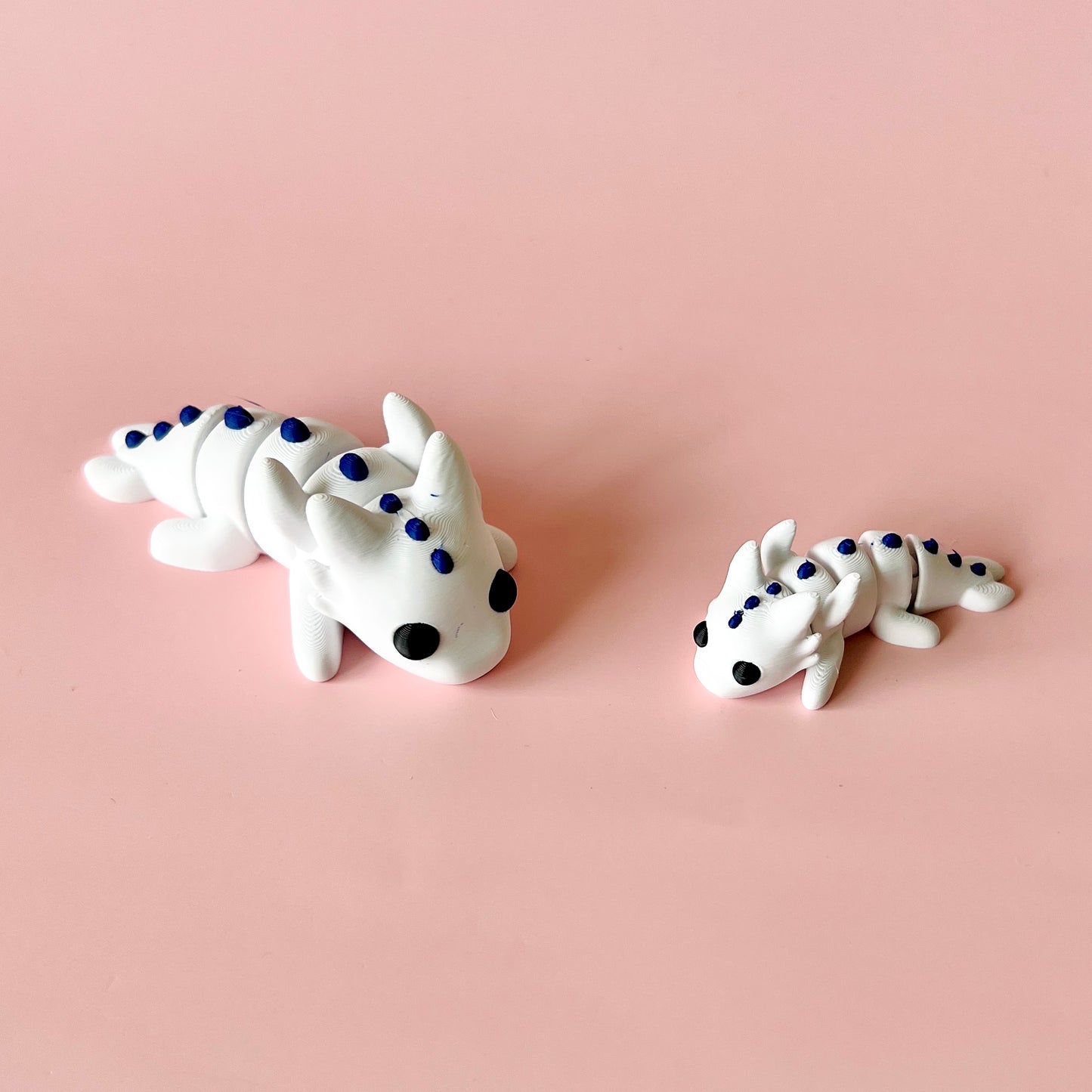 Two whimsical white creatures with blue spots, posed against a soft pink background.