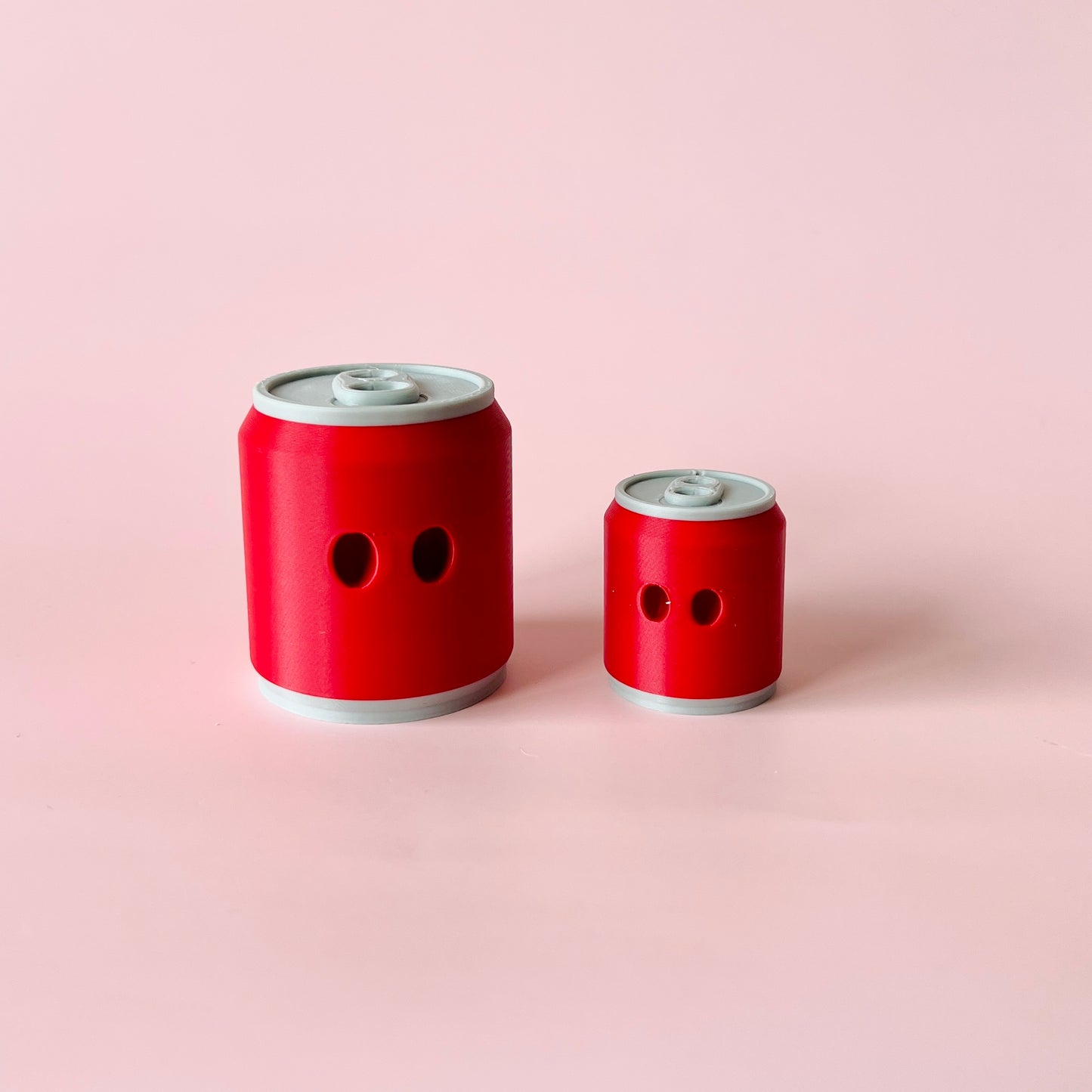 Two red containers with gray tops and circular openings, set against a soft pink background.