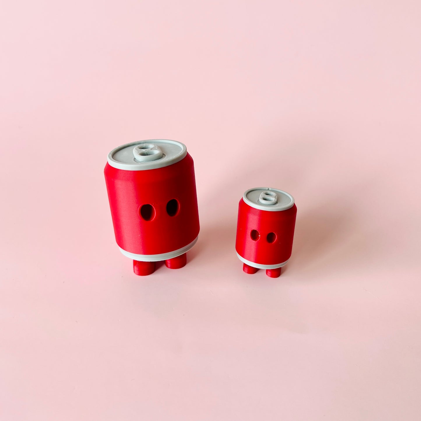 Two playful, red, cylindrical shapes with eyes and small feet, set against a soft pink background.