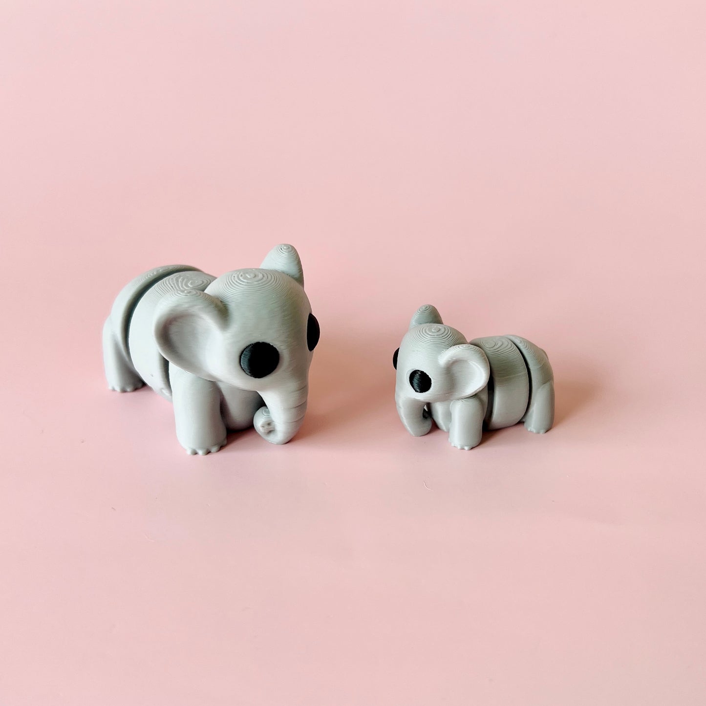 Two gray elephant figures, one large and one small, with round features and black eyes, set against a pink background.