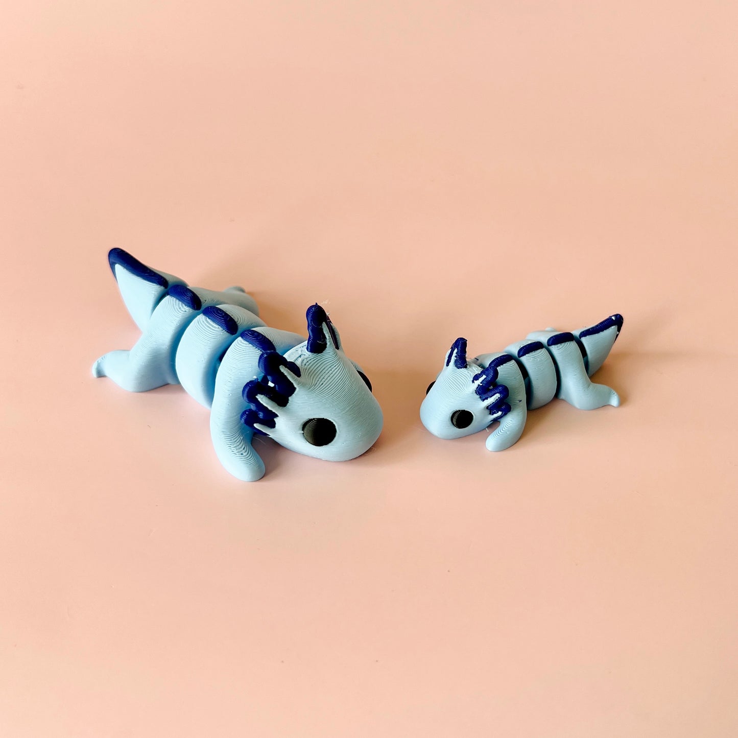 Two cute, blue creatures with dark blue accents, one larger and one smaller, set against a soft pink background.