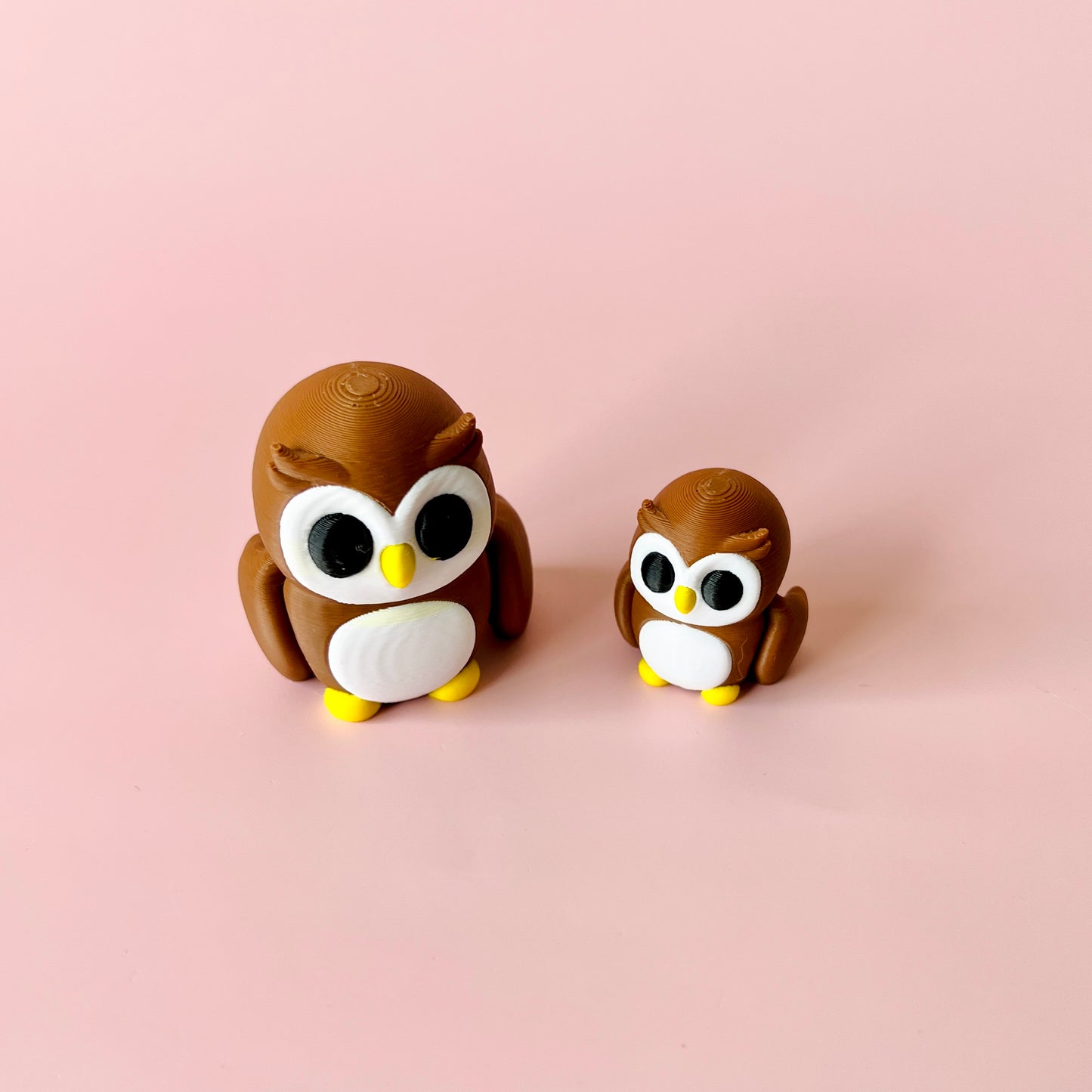 Two cute, brown owls with big eyes and yellow accents, one large and one small, against a soft pink background.
