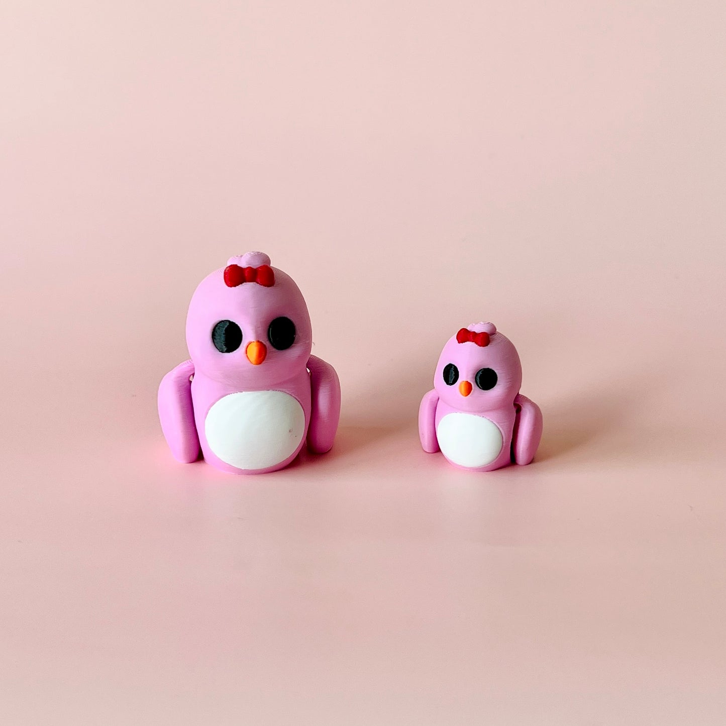 Two cute pink birds, one larger with a red bow, and a smaller one, both with black eyes and white bellies, on a soft pink bac