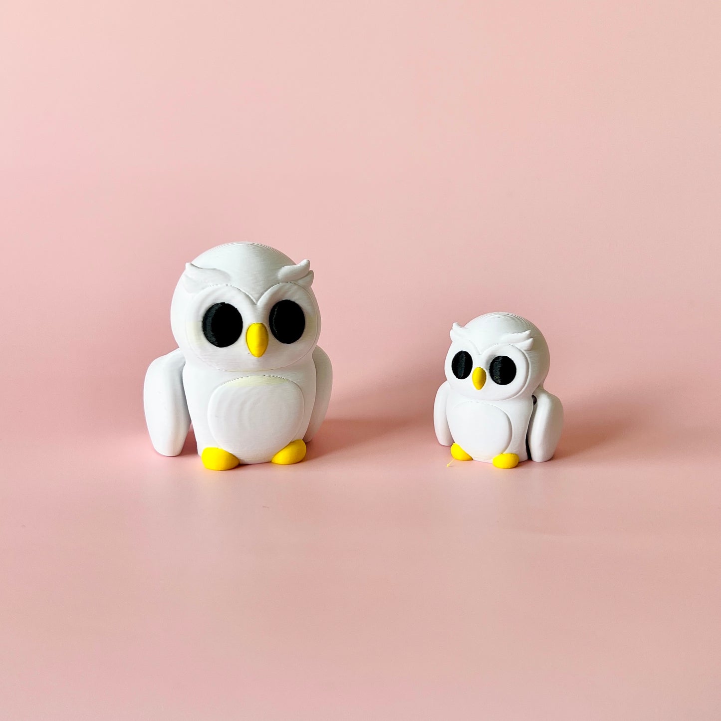 Two cute, white owls with yellow beaks and feet, set against a soft pink background. The larger owl is on the left.