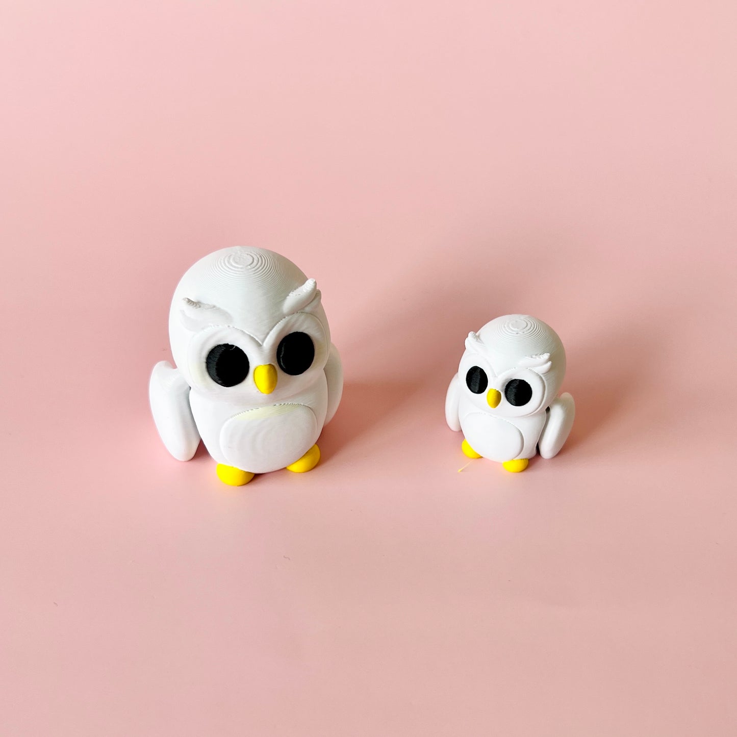 Two white owl figures, one larger with black eyes and yellow accents, set against a soft pink background.