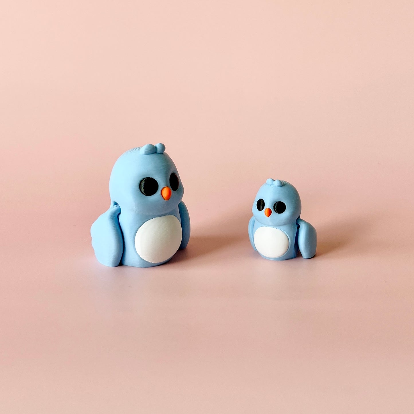 Two blue, stylized birds with round bodies and contrasting orange beaks, set against a soft pink background.