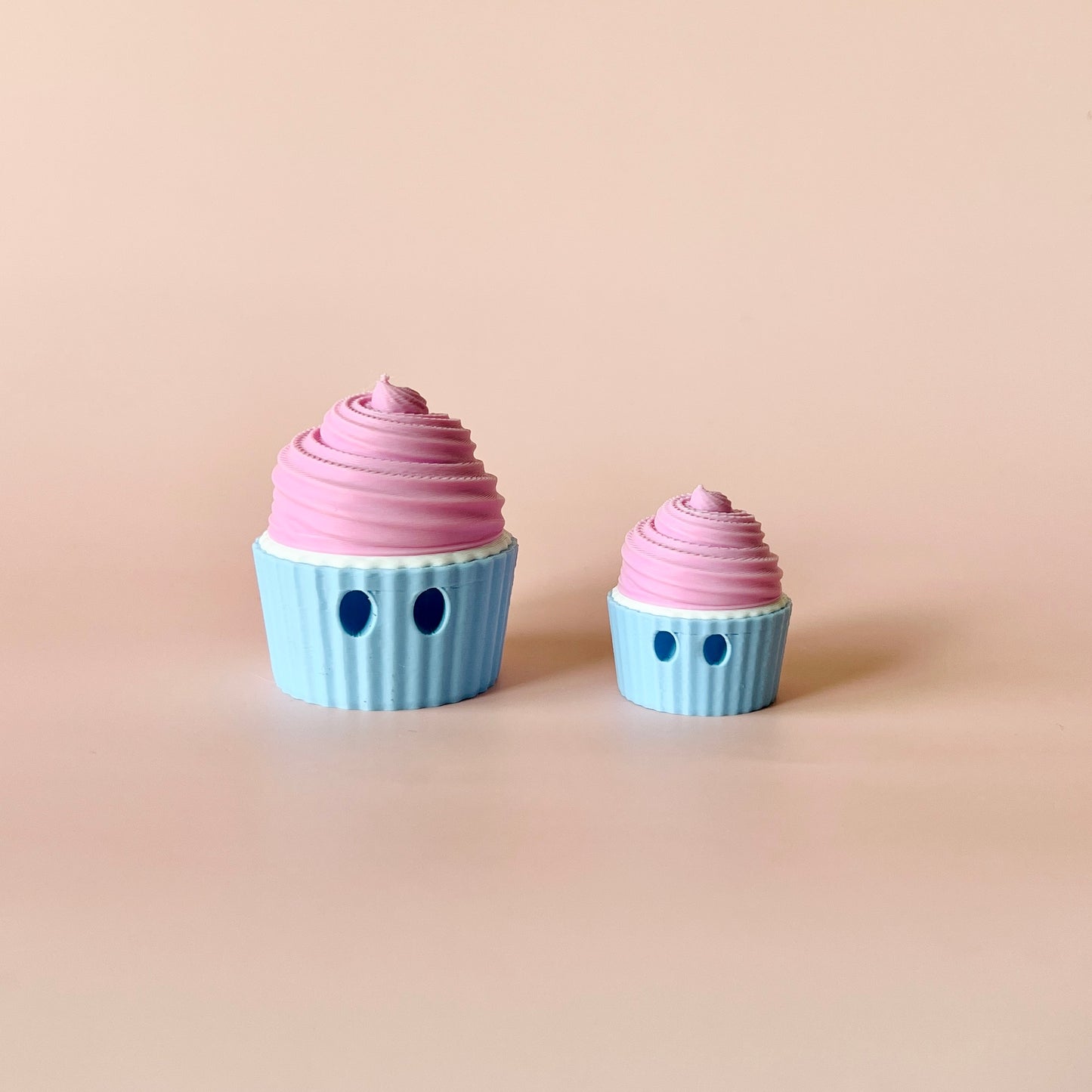 Two playful, pastel-colored cups with pink swirls, one larger than the other, set against a soft beige background.