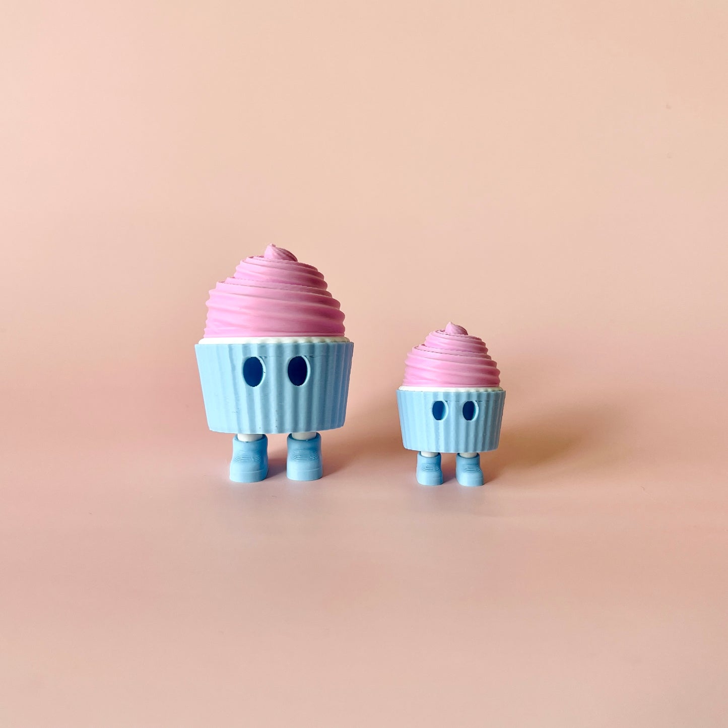 Two whimsical characters resembling desserts stand side by side against a soft pink background.