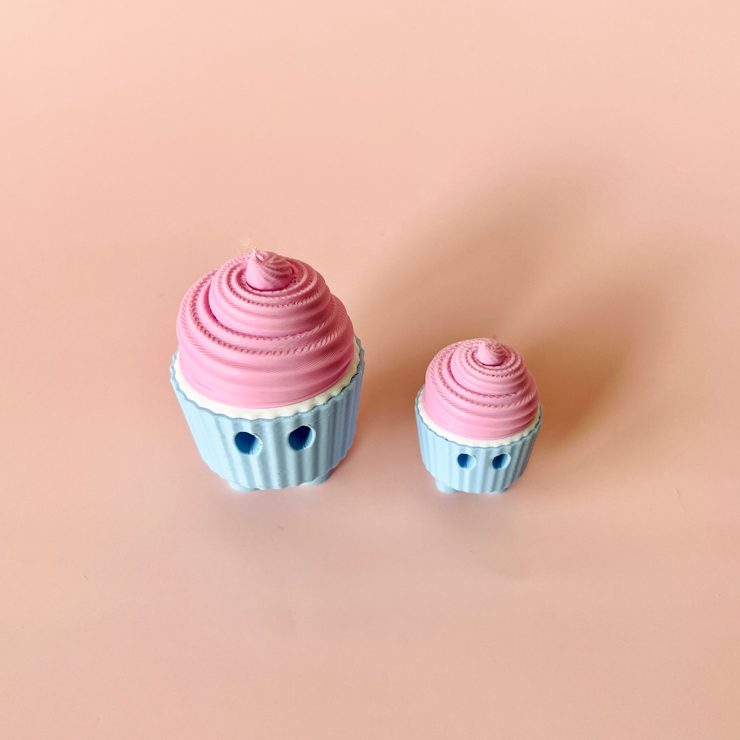 Two colorful cupcake figures, one large with pink frosting and one small, set against a soft pink background.