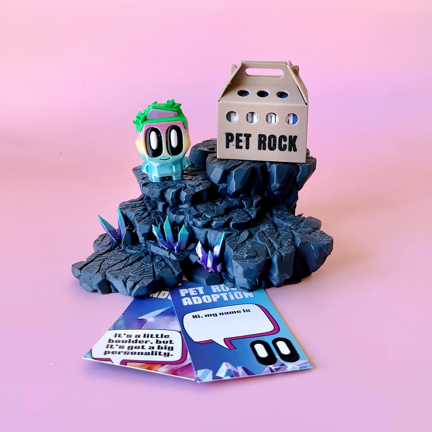 A whimsical creature with bright colors sits on a rocky base, surrounded by colorful crystals and an adoption card.