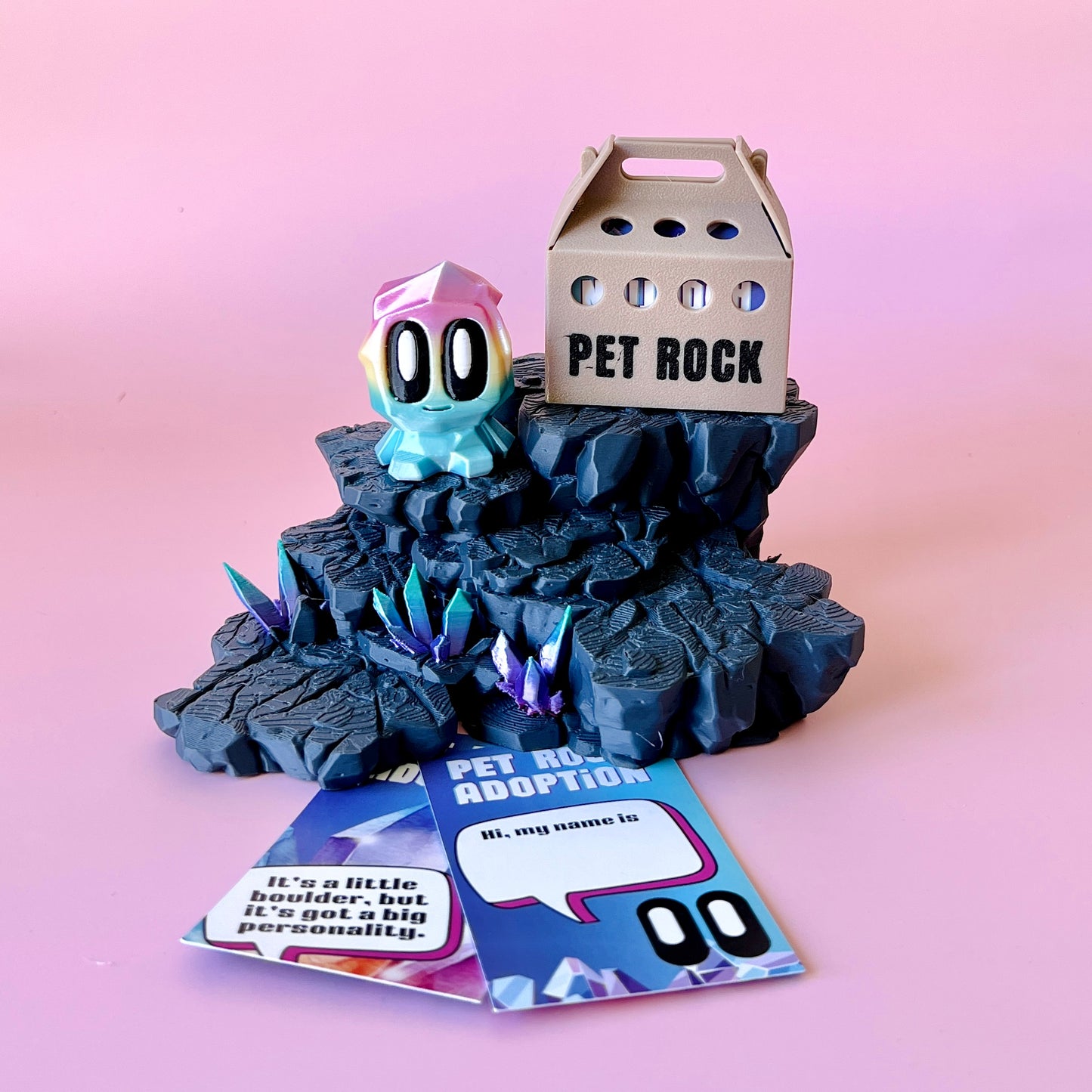 A colorful, whimsical creature perched on a rocky base with sparkling crystals, alongside a playful adoption card.