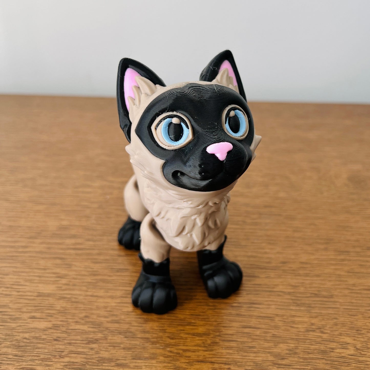 3D-printed Siamese cat figurine with vibrant colors, big blue eyes, and a playful expression, perfect for cat lovers.