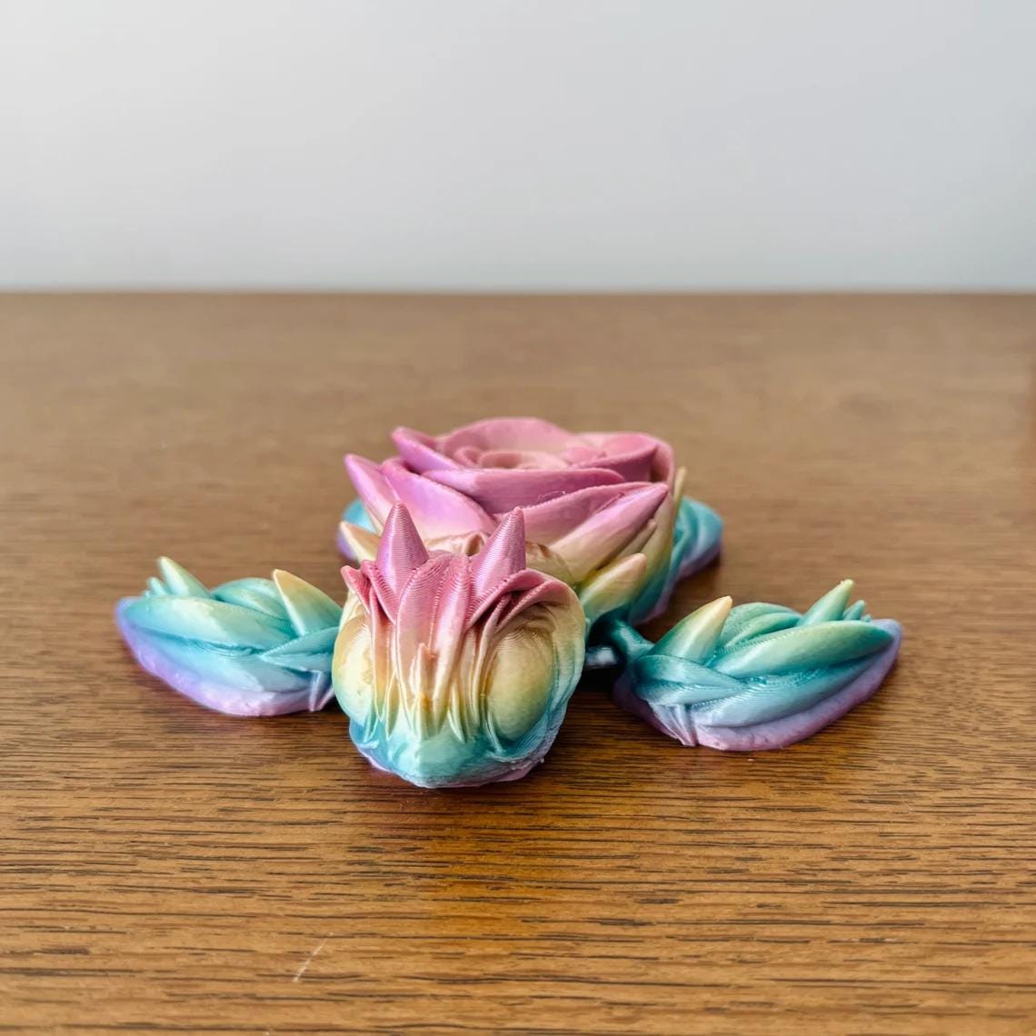 Colorful 3D-printed turtle with a rose for a shell, blending shades of pink, purple, and blue on a wooden surface.
