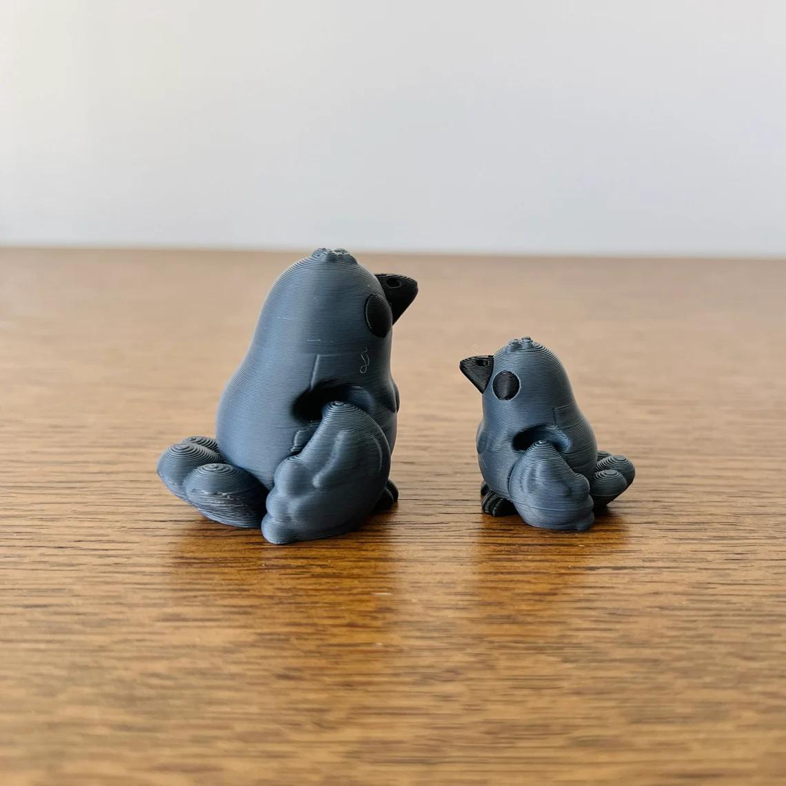 Two sleek, articulated crows in matte black, one larger and one smaller, resting on a wooden surface.