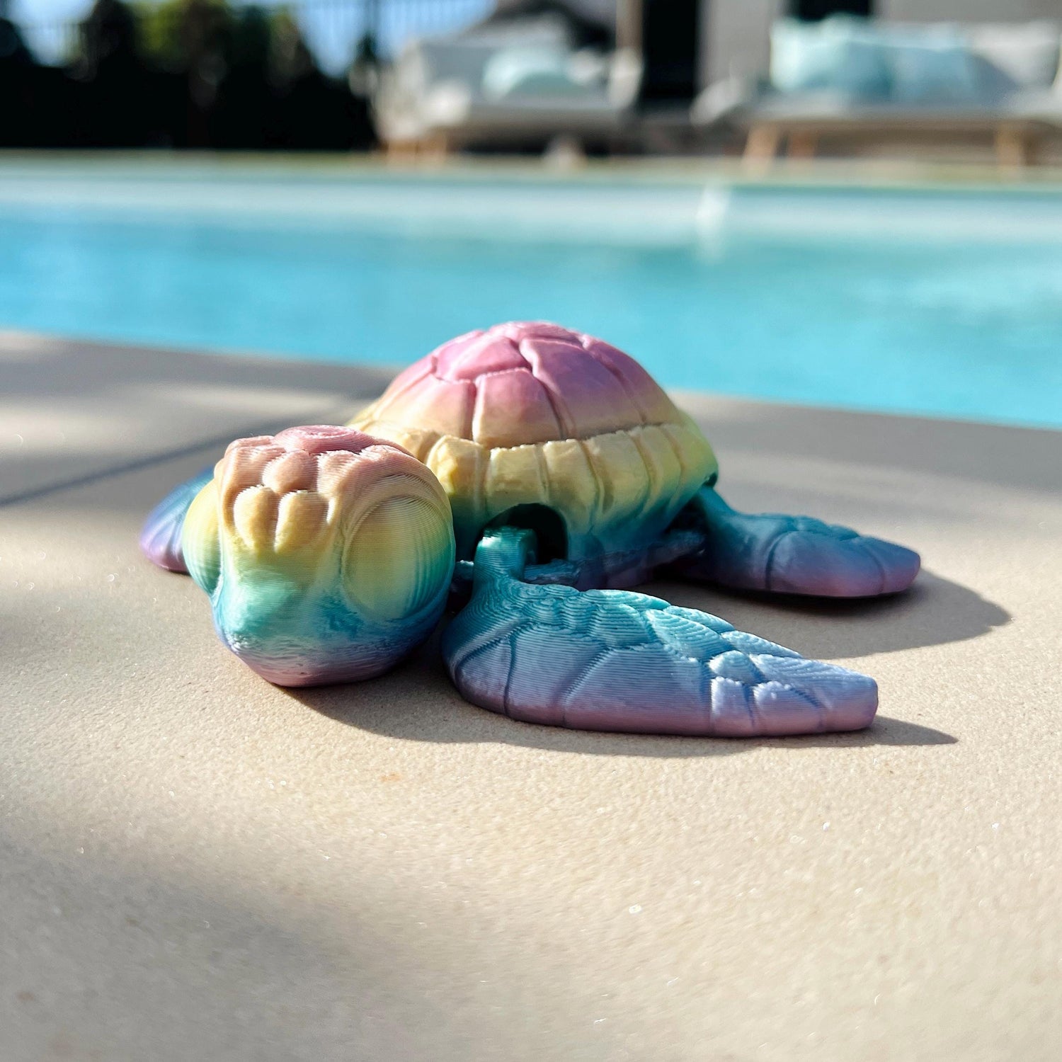 Colorful 3D-printed sea turtle resting on a surface, with intricate details and a serene pool backdrop.