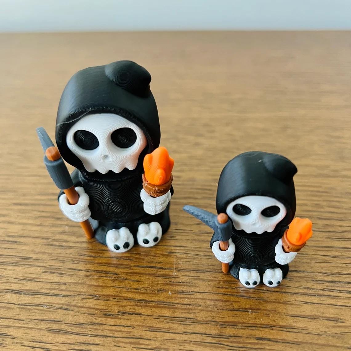 Adorable mini Grim Reapers in black robes, holding a torch and scythe, with cute shoes and expressive skull faces.