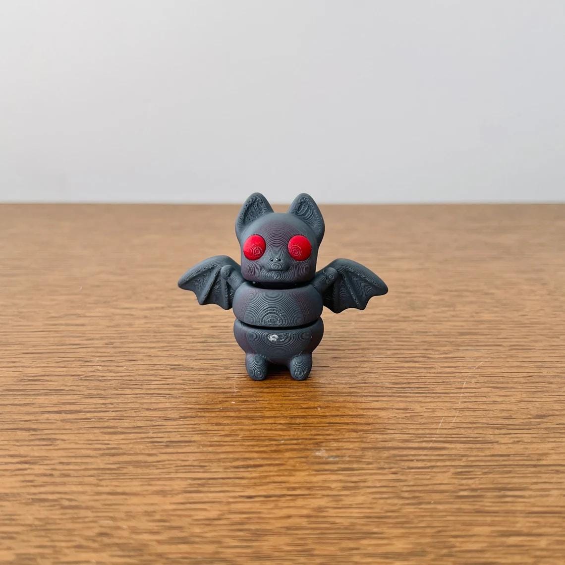 Articulated black bat with red eyes, perfect for sensory play and eco-friendly fun, set against a wooden surface.