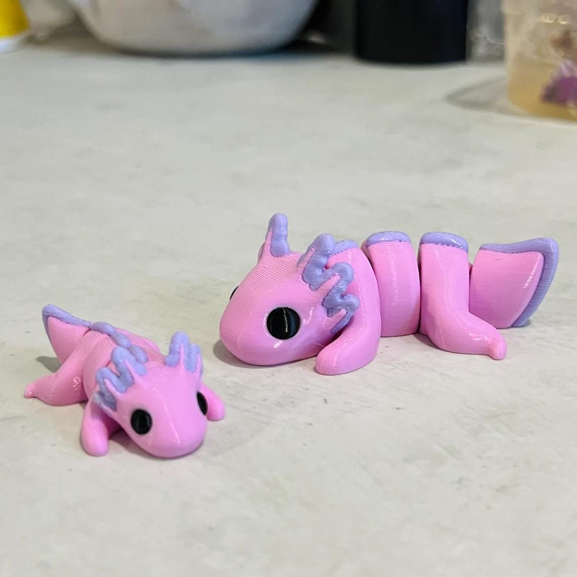Two adorable pink axolotls, one smaller and one larger, with detailed features and a playful, articulated design.