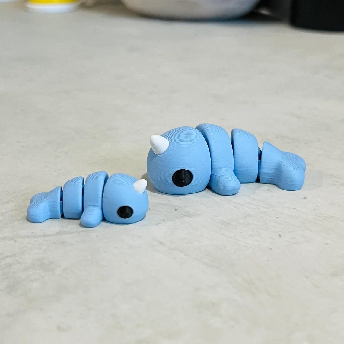 Charming blue narwhals with articulated bodies, featuring white tusks, resting on a light surface. Perfect for sensory play.