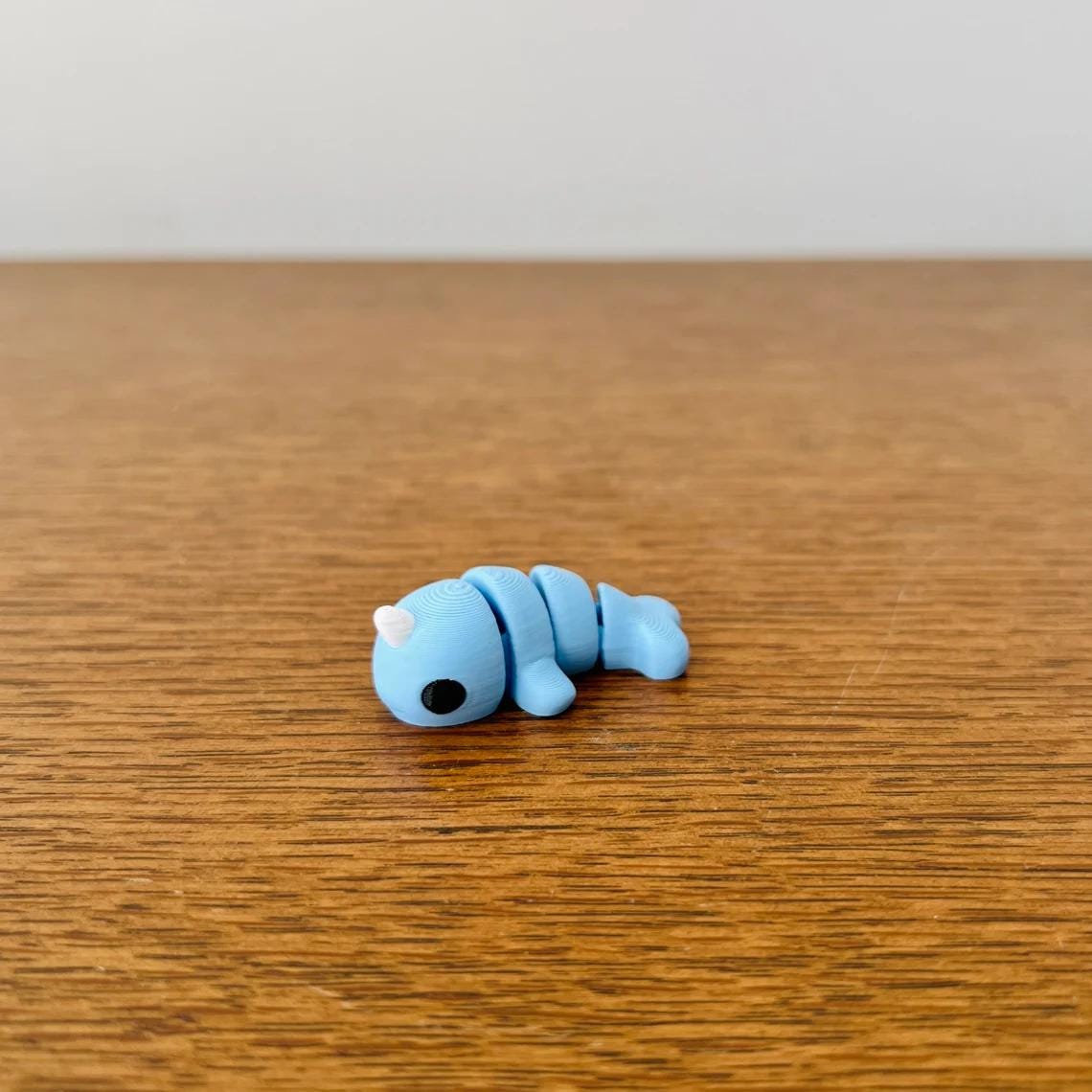 3D printed blue narwhal with a playful expression, resting on a wooden surface, perfect for sensory enjoyment.