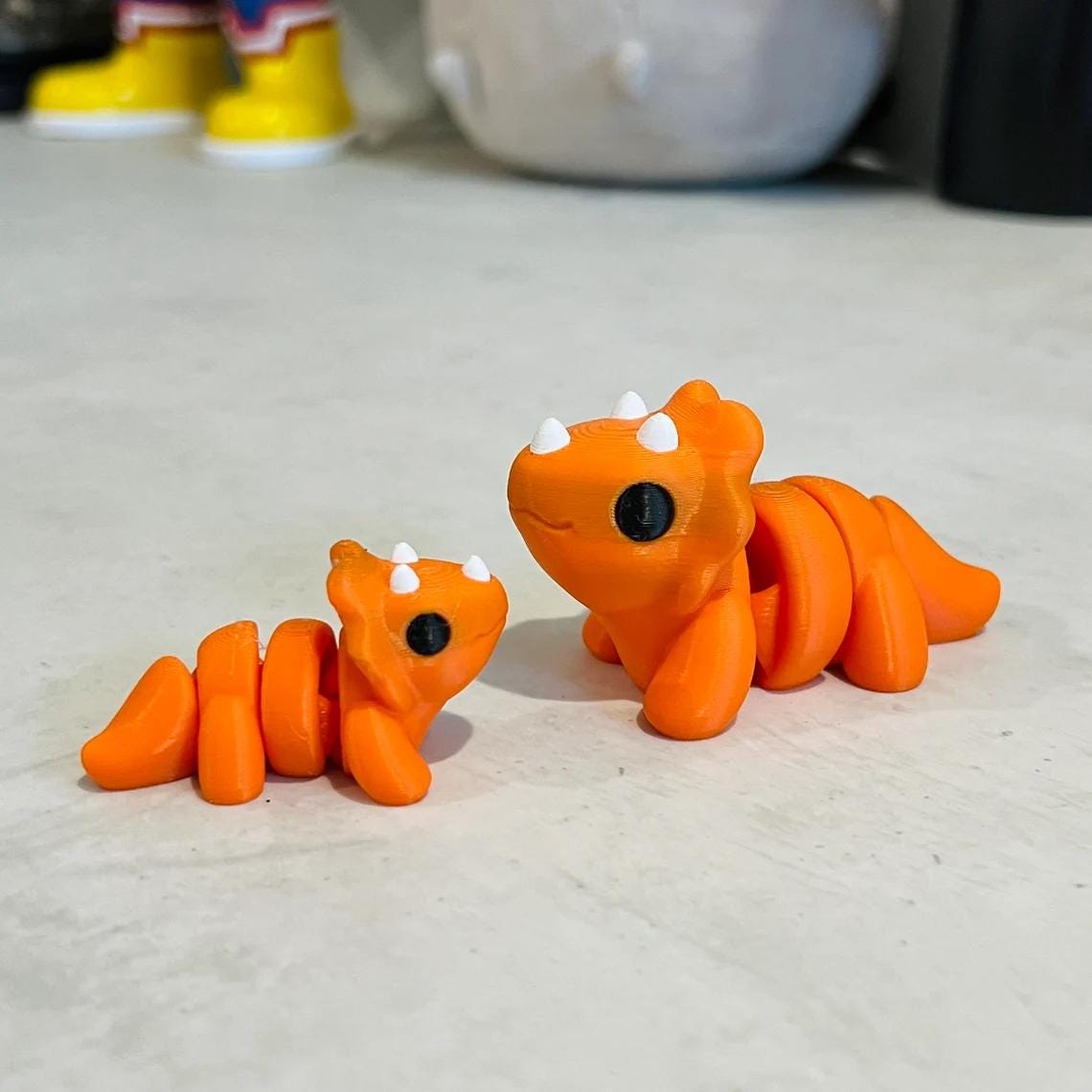 Adorable orange Triceratops figures, one large with white spikes and a smaller one, set against a neutral background.