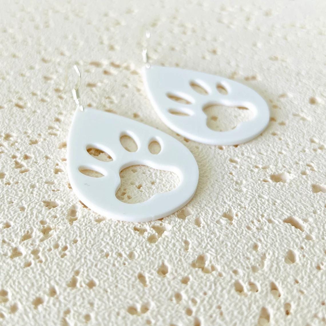 White paw print dangle earrings with sterling silver hooks, featuring a playful design, perfect for everyday wear.