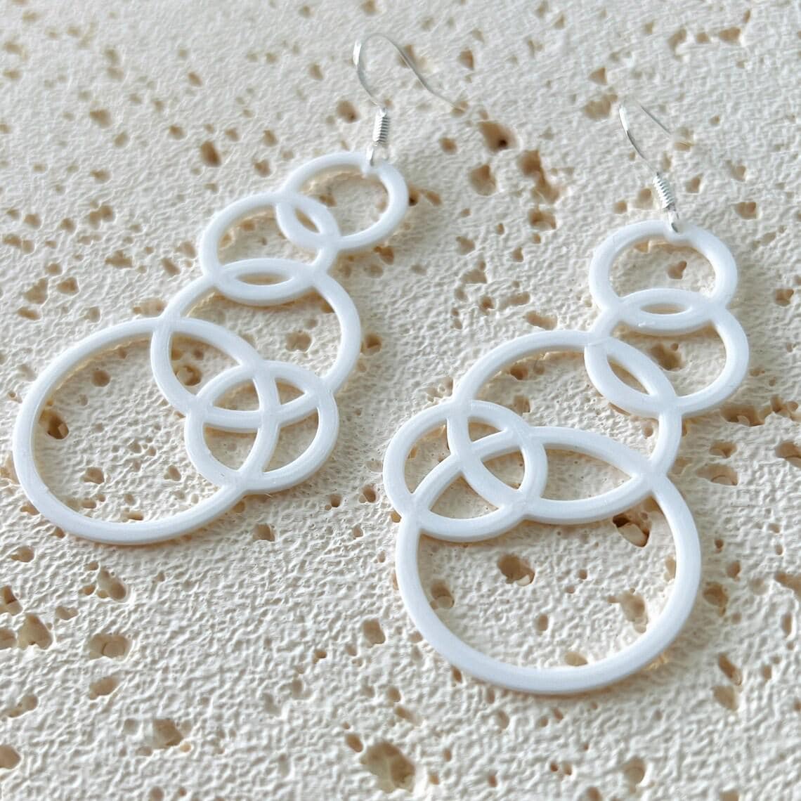 White bubble dangle earrings with multiple interlocking circles, hanging from sterling silver hooks, on a textured background