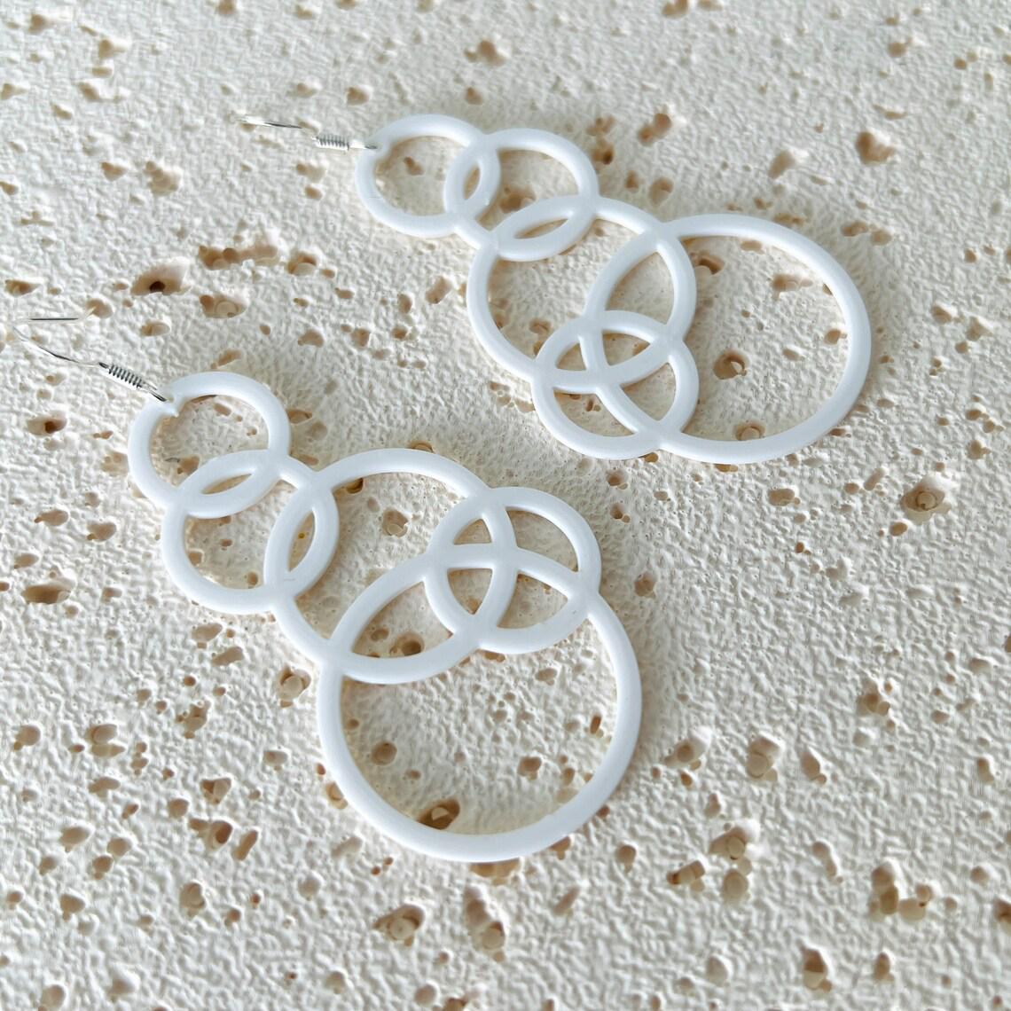 White bubble dangle earrings with multiple interlinked circles, hanging from sterling silver hooks on a textured surface.