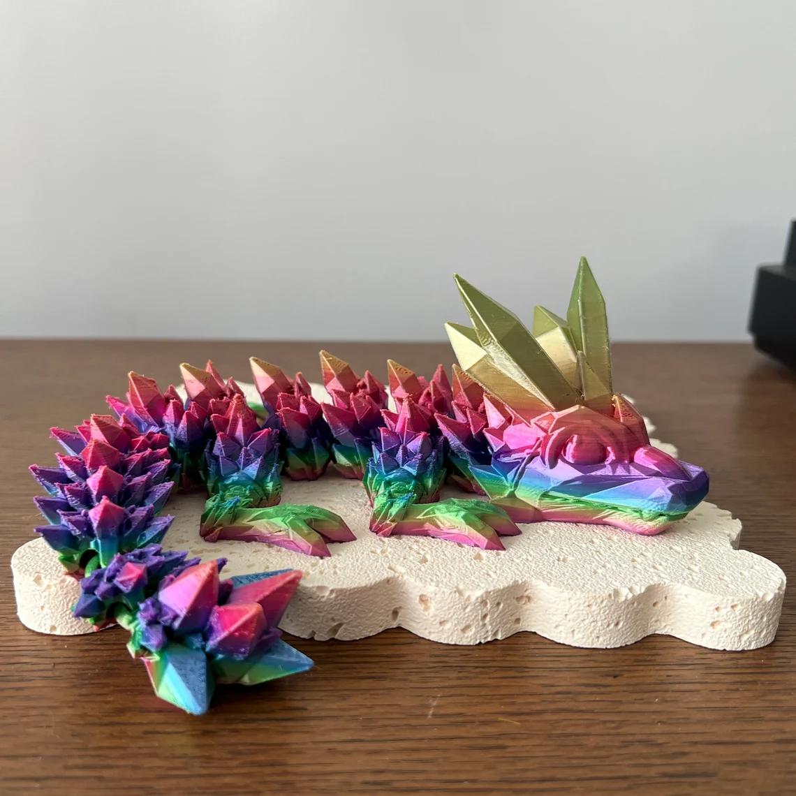 Vibrant 3D printed dragon with colorful spikes and golden crystal-like accents, resting on a textured base.