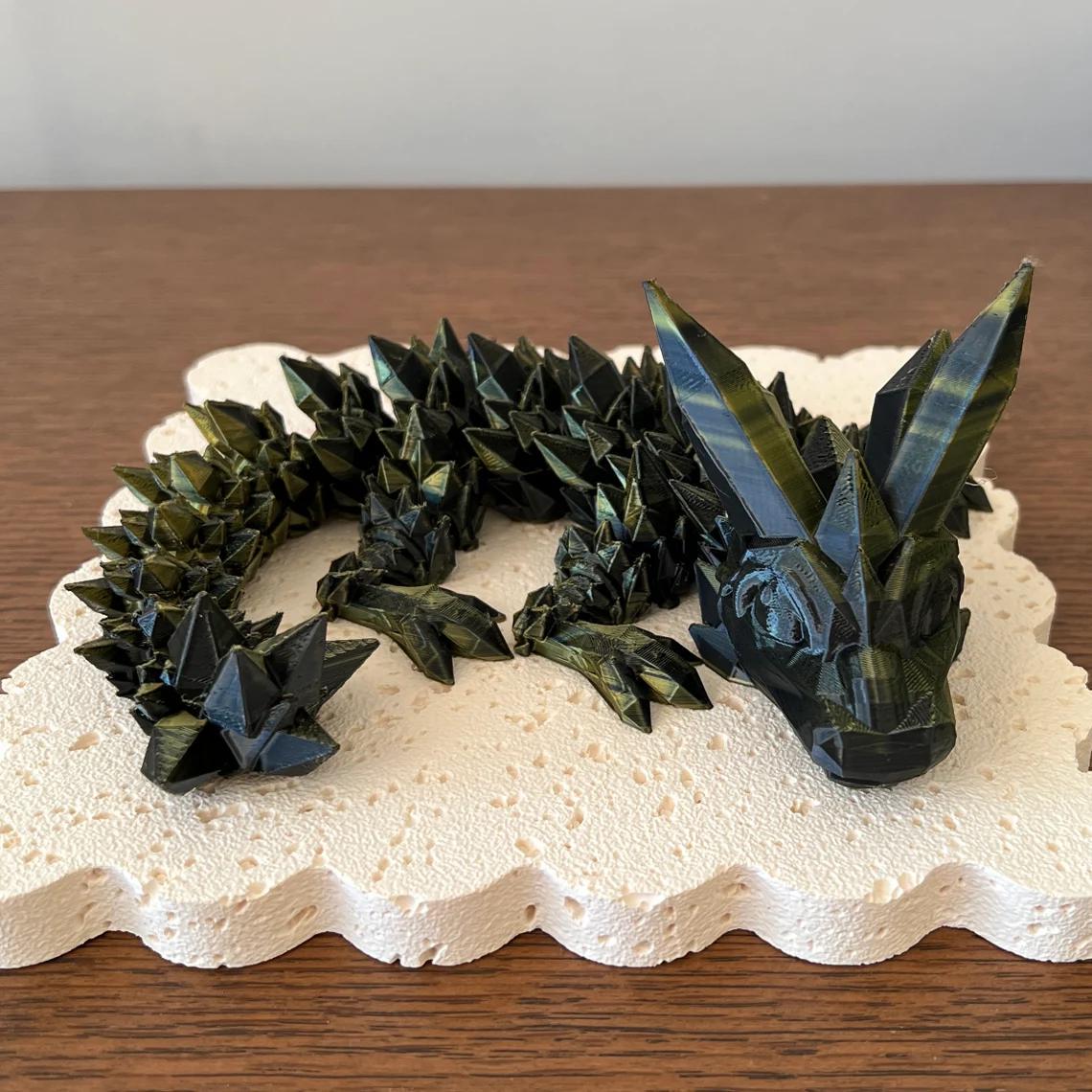3D printed crystal dragon with sharp, geometric features resting on a textured, light-colored base. Unique and customizable.