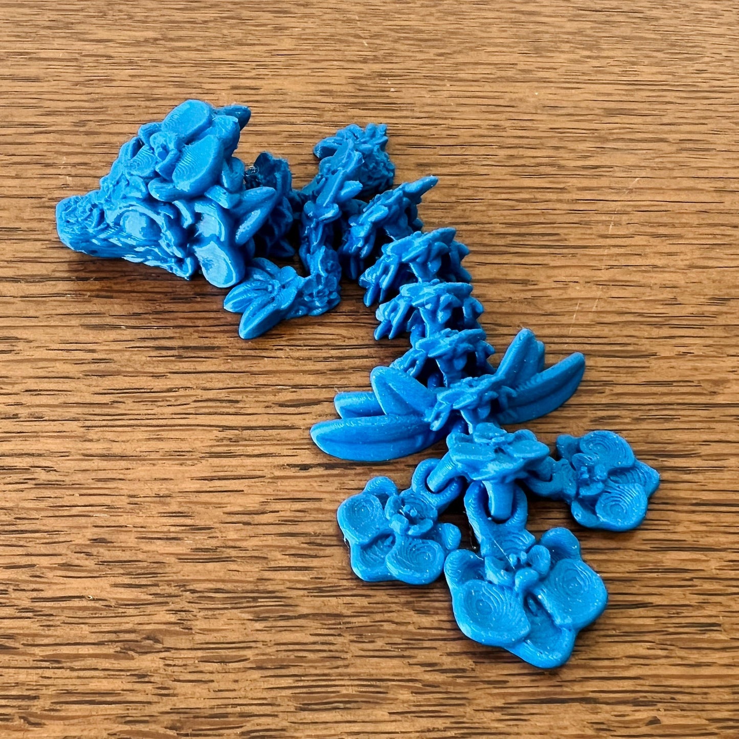 Whimsical blue Orchid Dragon Tadling, featuring intricate floral details, lies gracefully on a wooden surface.