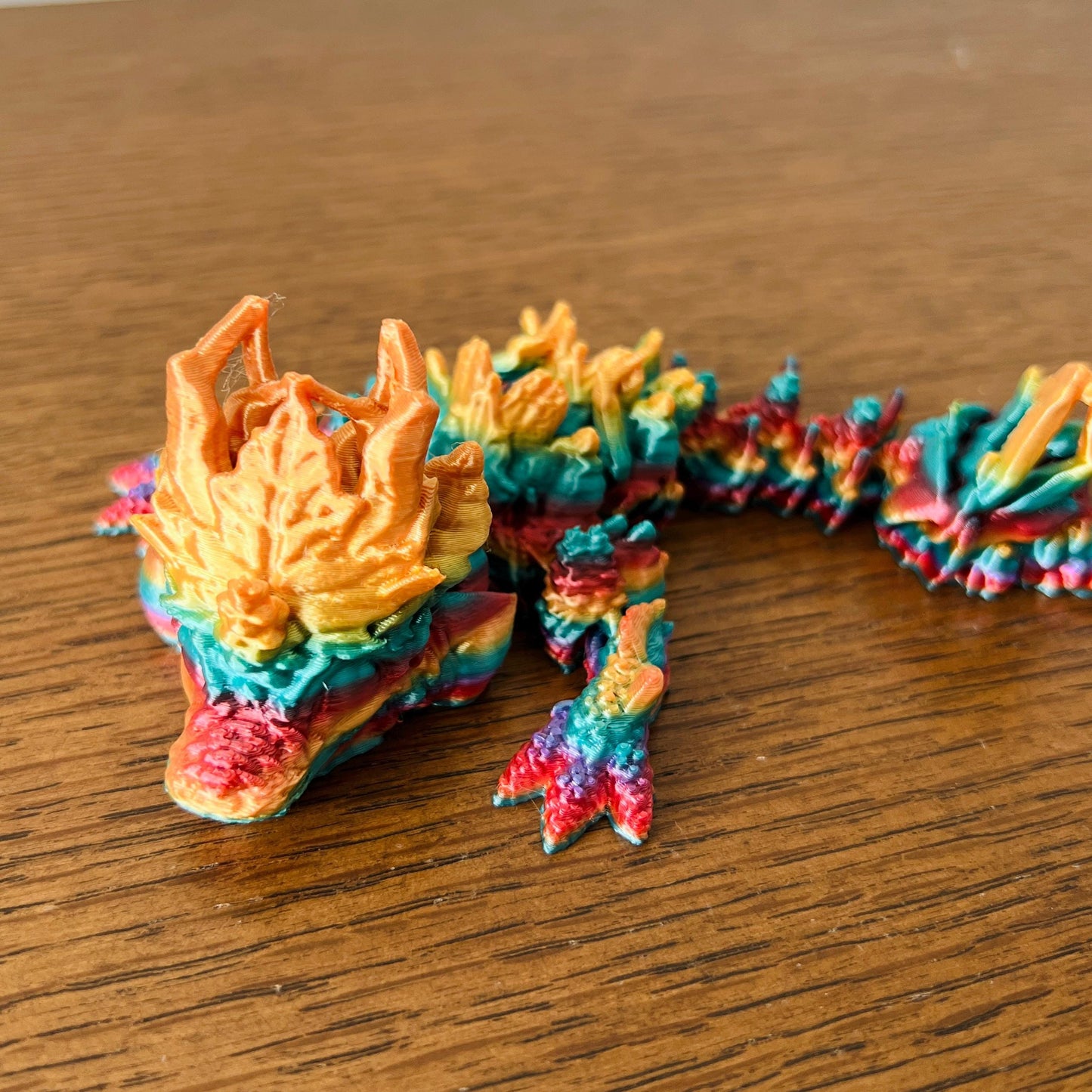 Colorful dragon with intricate autumn leaf textures, showcasing vibrant hues of orange, green, and red on a wooden surface.