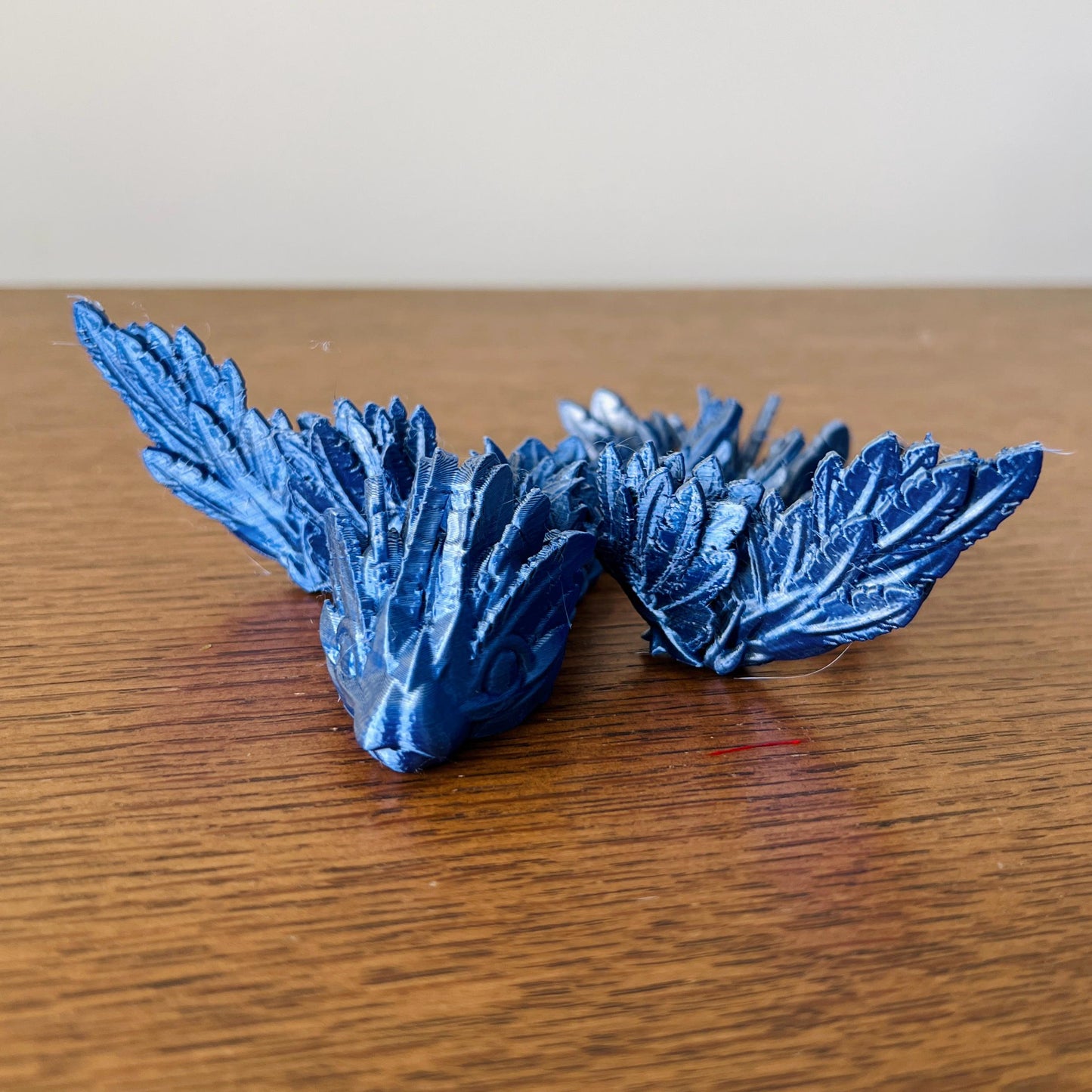 A sleek blue dragon with intricate scales and striking wings rests elegantly on a wooden surface.