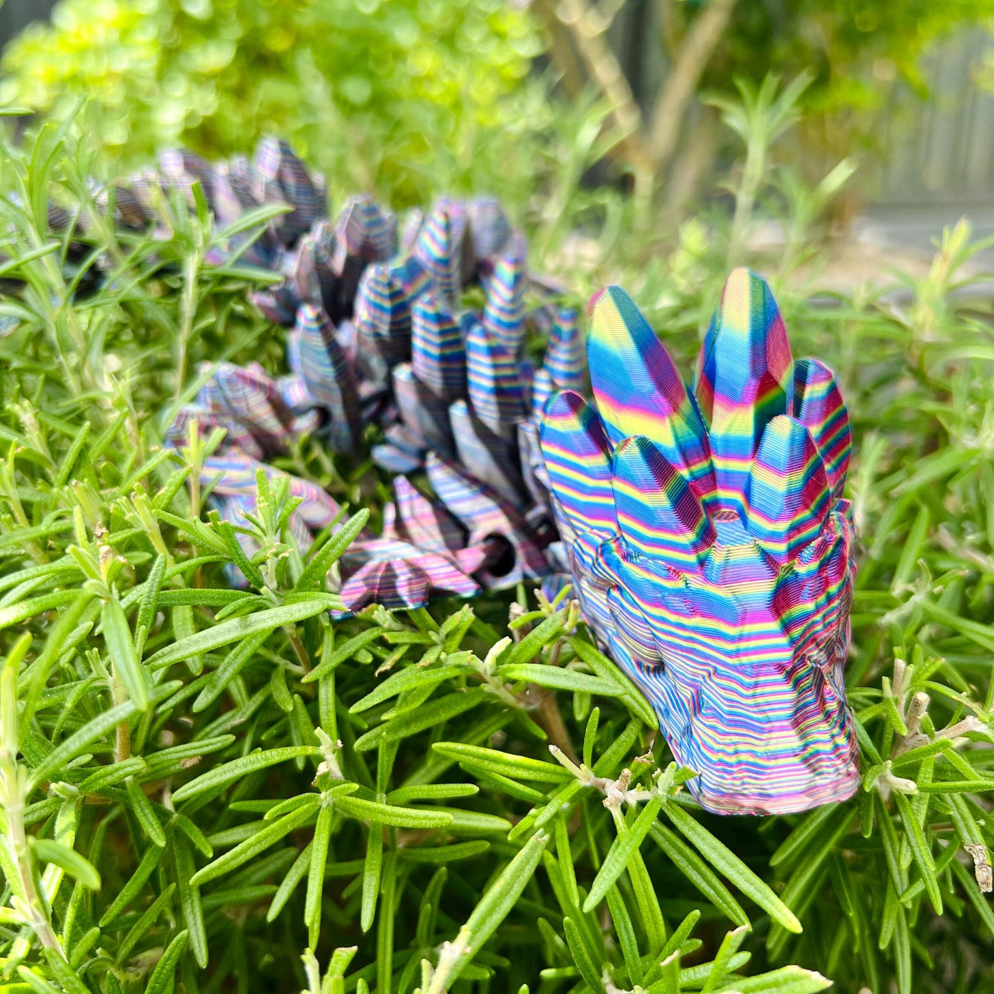 A vibrant, intricately detailed dragon with a gemstone-inspired design peeks through fresh green foliage.