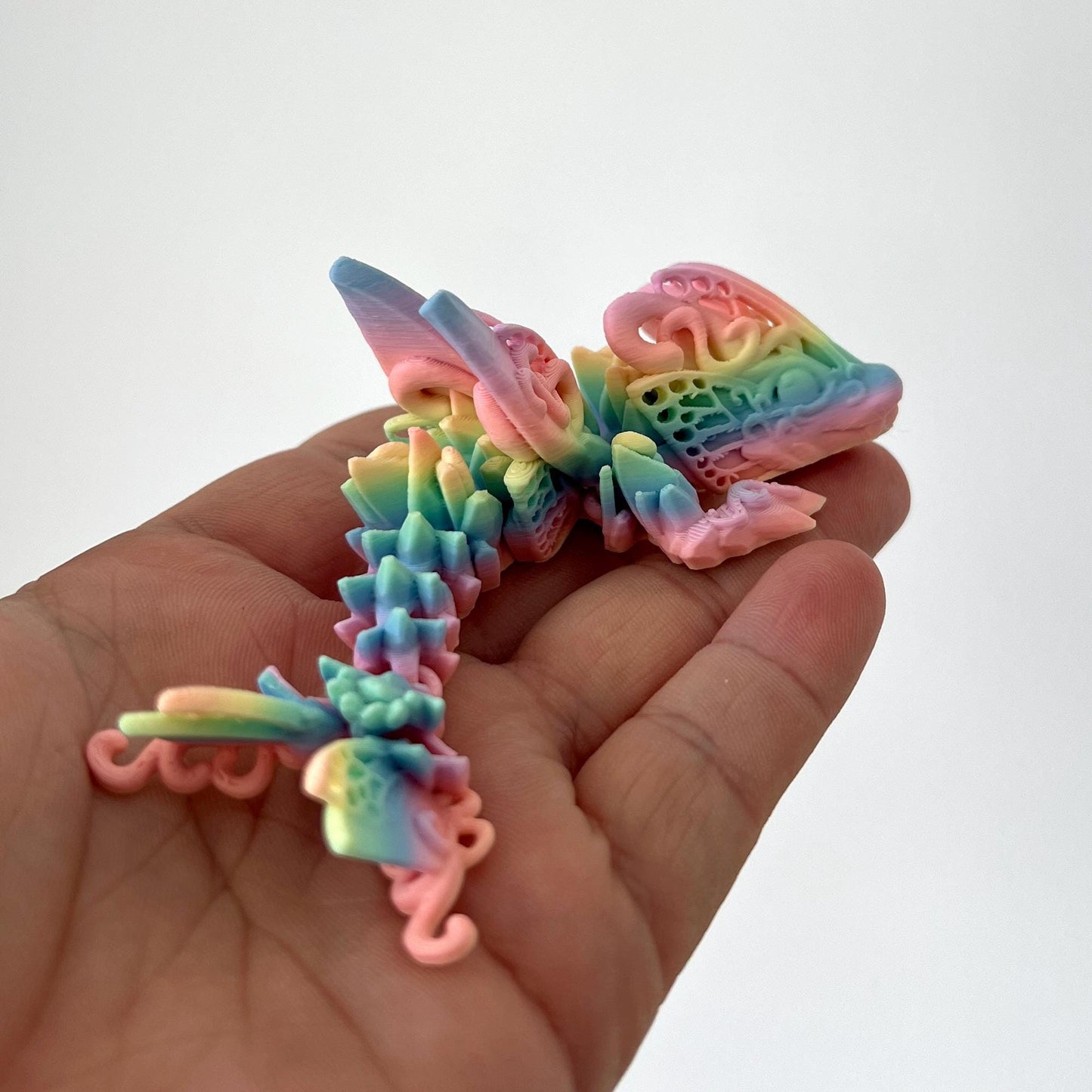 Colorful, articulated creature with butterfly wings and dragon features, resting in a hand against a plain background.