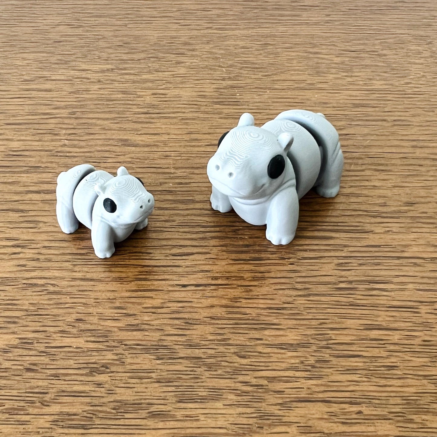 Two articulated gray mini hippos with black eyes on a wooden surface, offering a playful tactile experience.