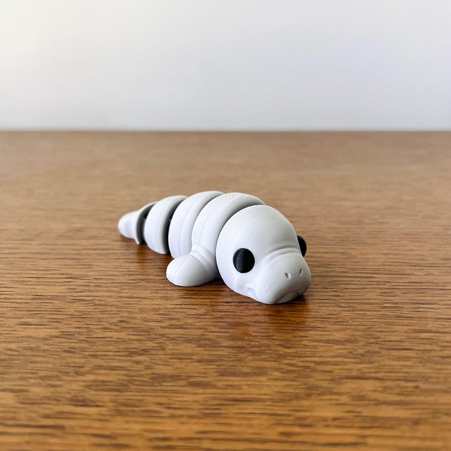 Adorable articulated mini manatee in soft gray, perfect for sensory play and stress relief, resting on a wooden surface.