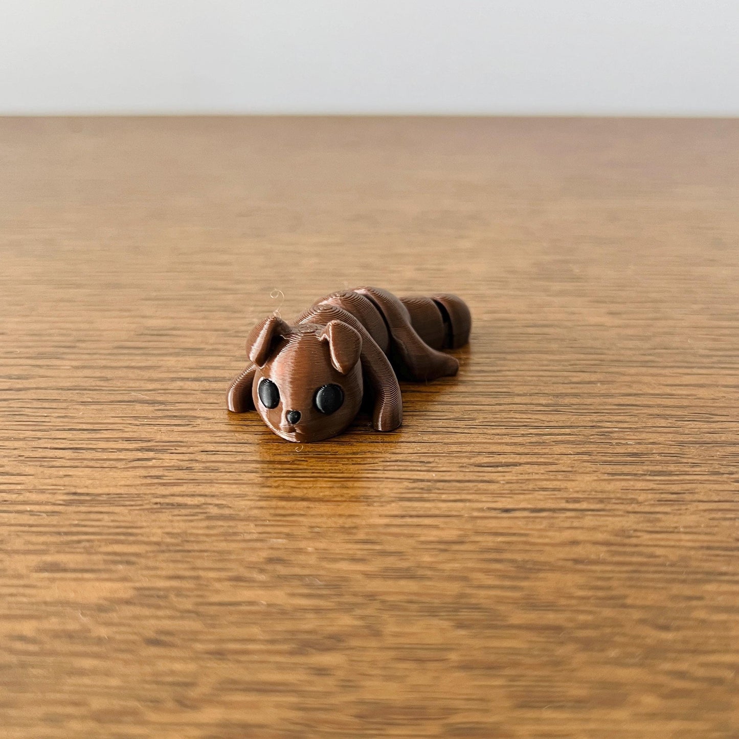 Adorable mini brown puppy with big black eyes, resting on a wooden surface, perfect for sensory play and stress relief.