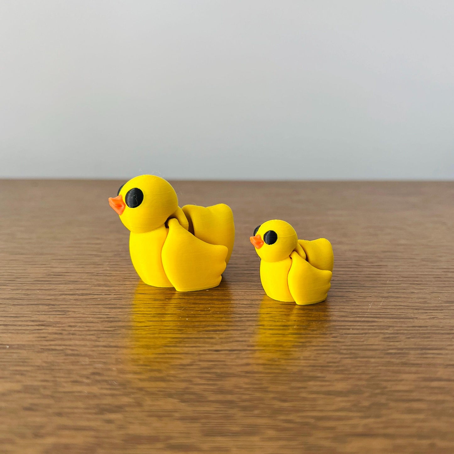 Two cheerful yellow ducks, one larger and one smaller, with bright orange beaks and playful black eyes on a wooden surface.